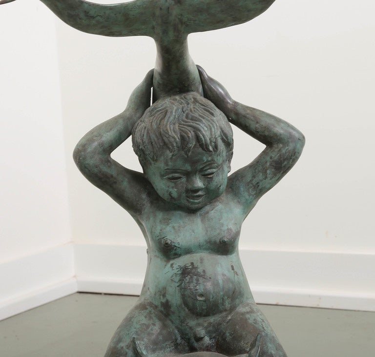 Bronze statues with cherub faced putti riding stylized dolphins on black composition bases.