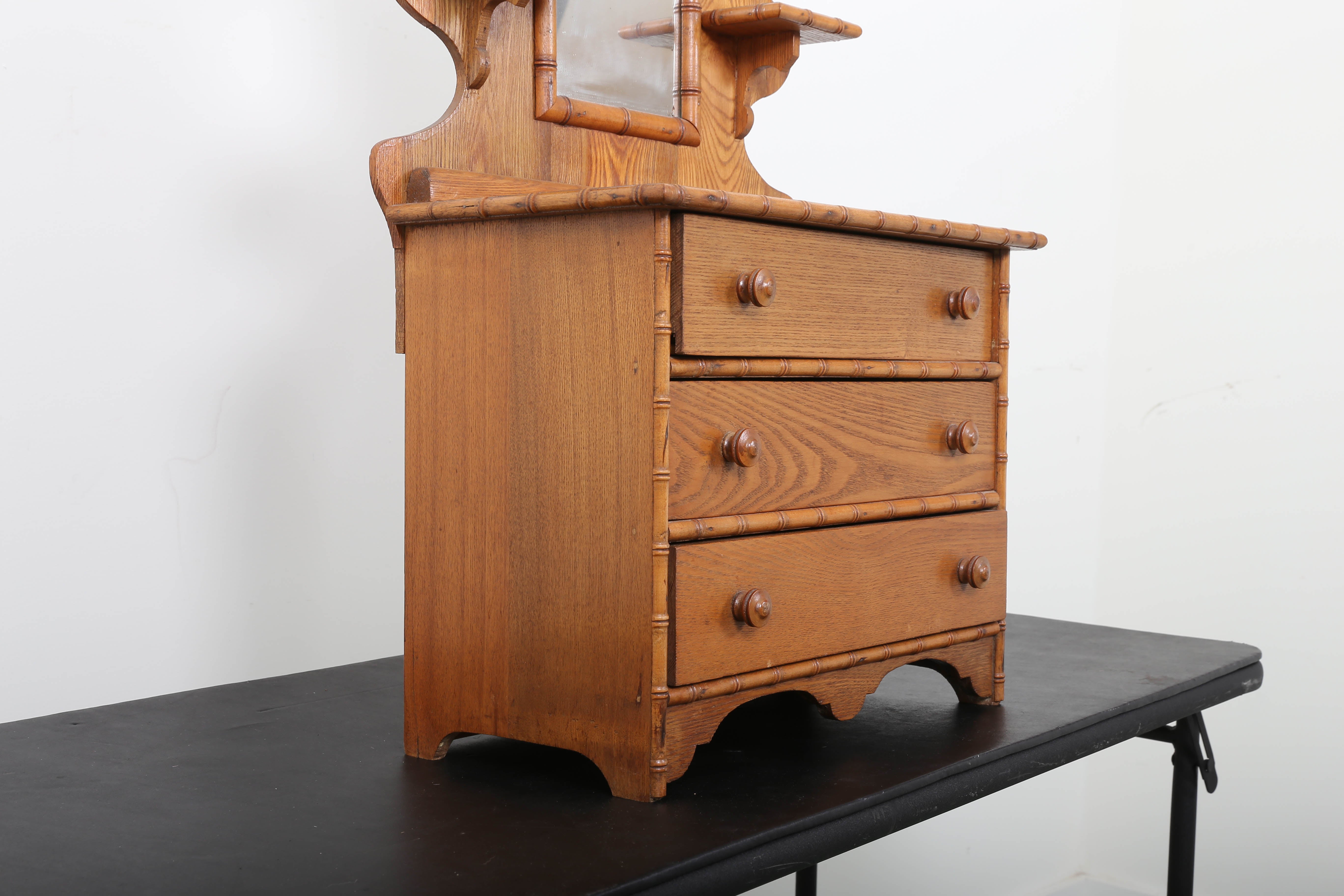 Figural hardwood dresser. Three drawers, wood pulls, faux bamboo trim; two small shelves either side of mirror.