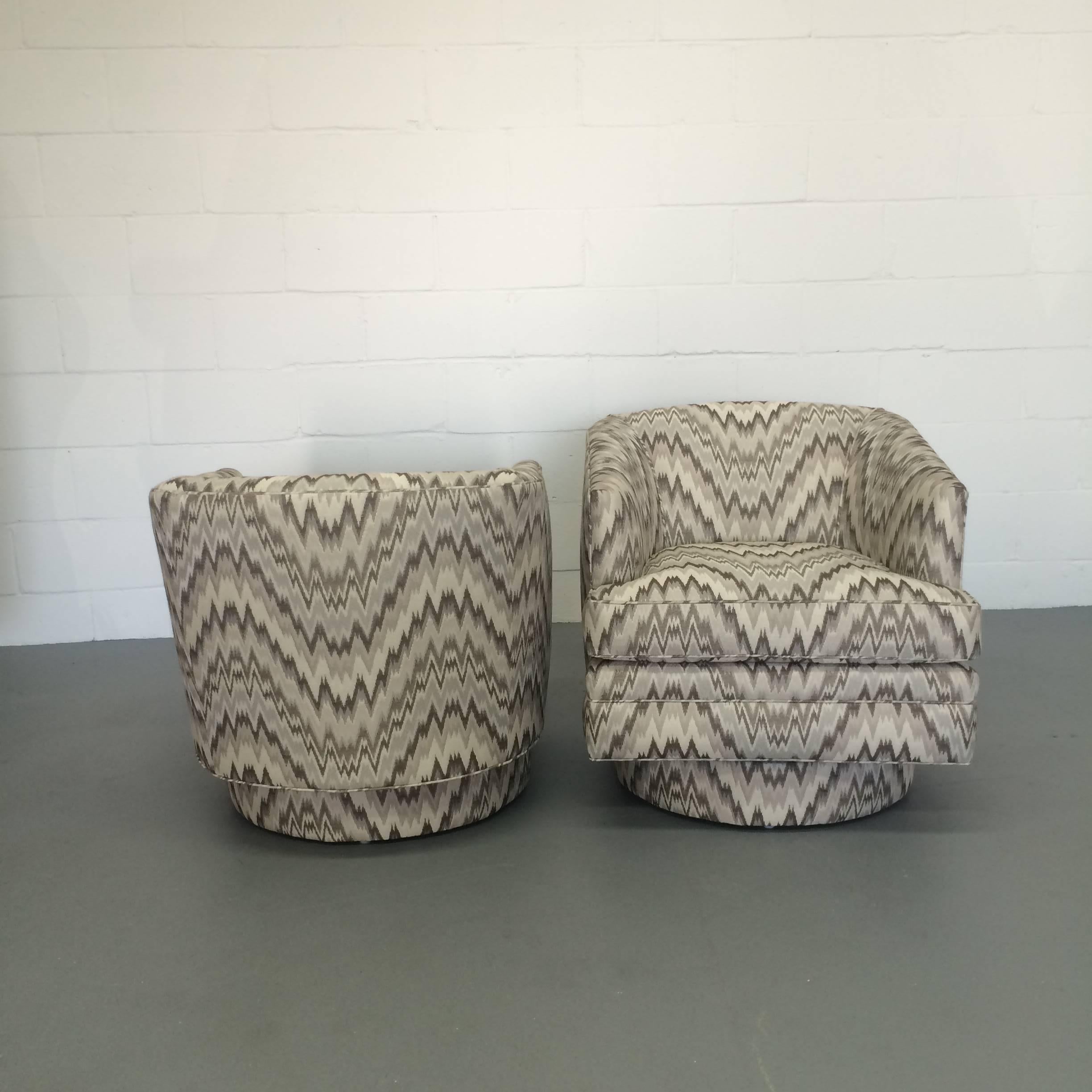 A very special pair of freshly upholstered Mid-Century Modern swivel club chairs in a chevron print in hues of grays and creams. The pattern of the fabric is matching from the top all the way to the bottom of the plinth base. A wonderful size and