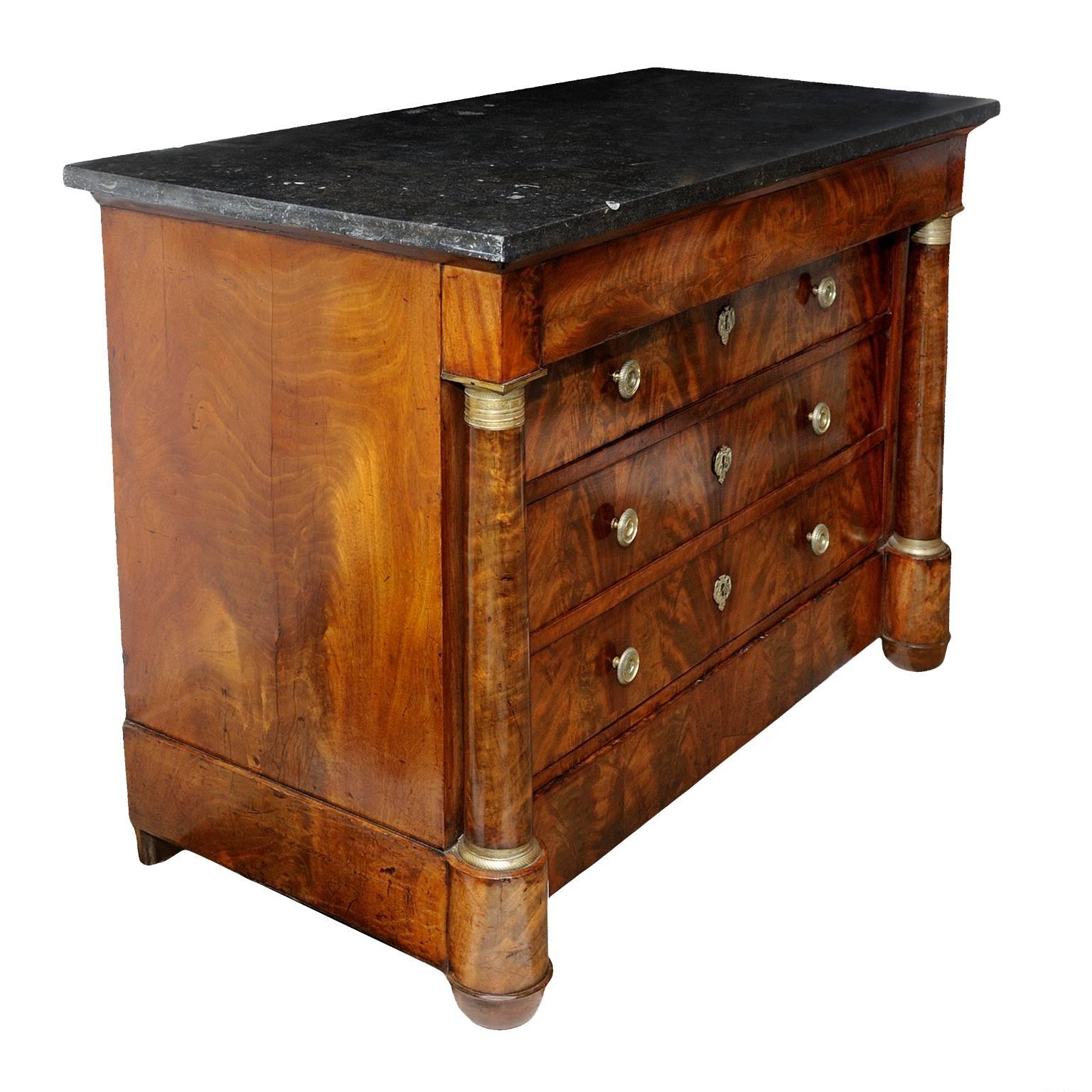 This is a very fine quality early 19th century, French Empire period flame mahogany five-drawer Napoleonic Commode, retaining its original black fossil marble top and original handles, escutcheons, locks and mounts, circa 1820. 

An absolutely