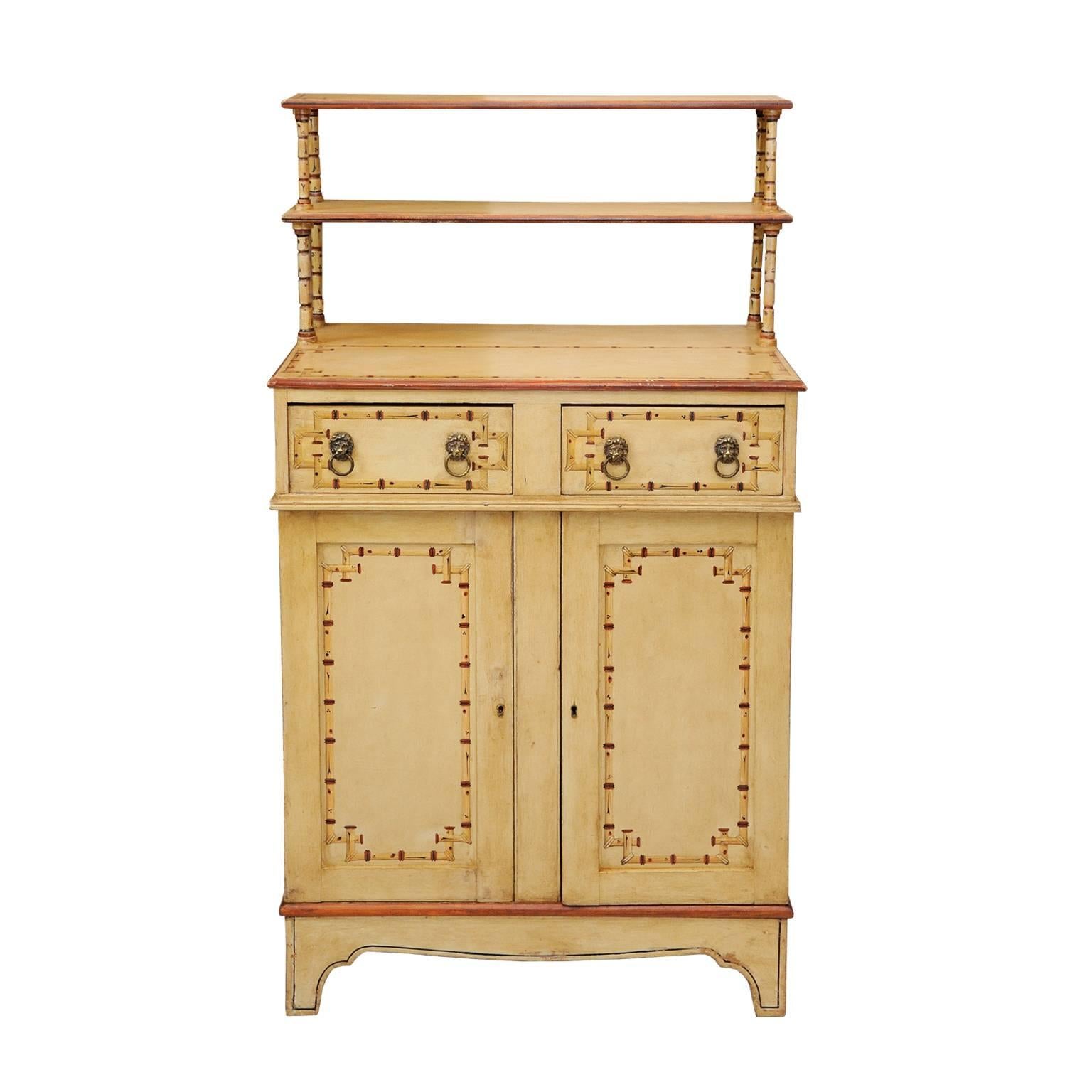 This is a rather wonderful English, early 19th century Regency painted faux bamboo chiffonier cupboard with later painted bamboo decoration.
Featuring an opening shelved cupboard with two draws above and a two-tier shelf at the top. Complete with