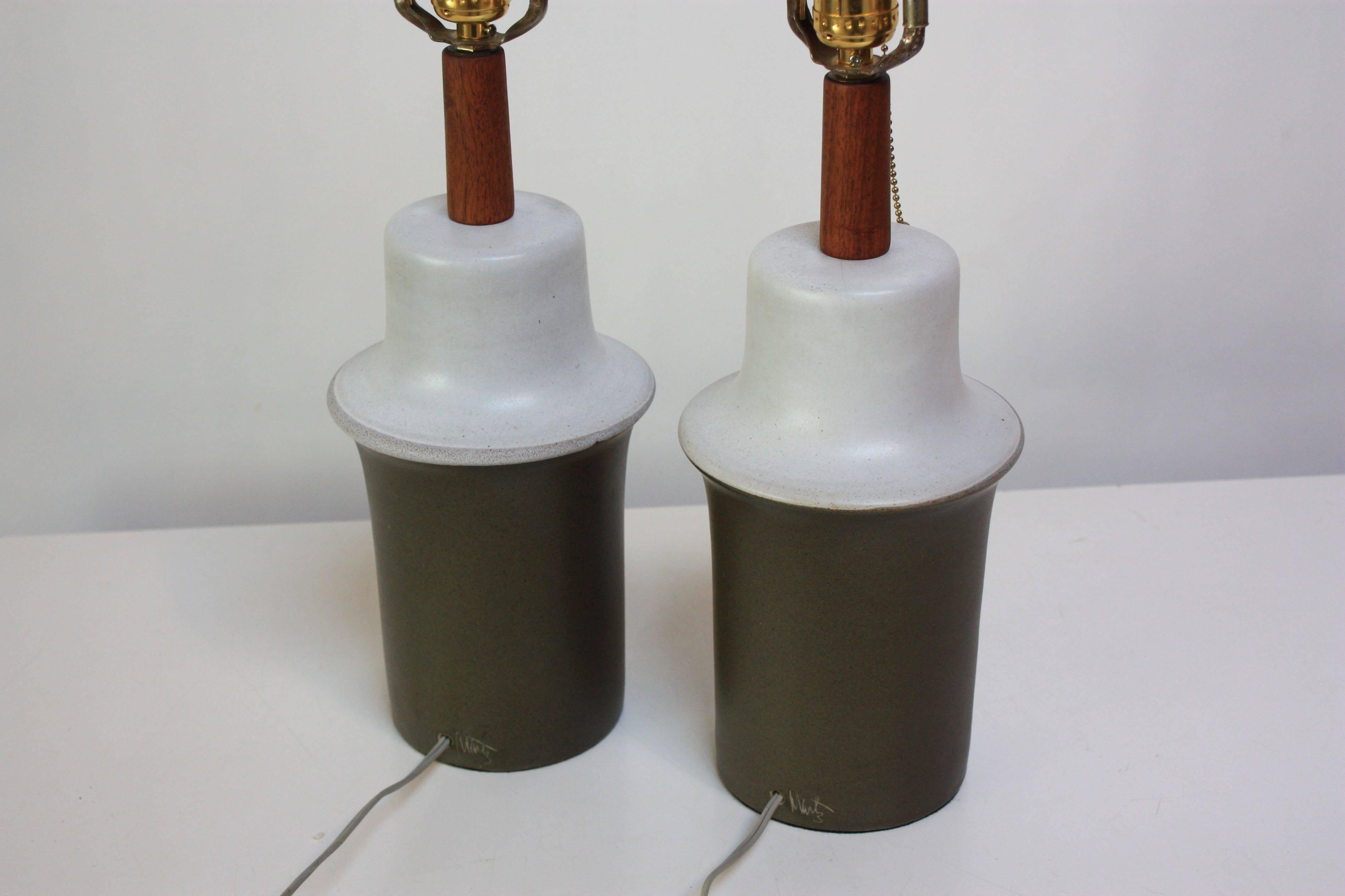 These ceramic lamps were designed by Gordon and Jane Martz for Marshall Studio featuring a two-tone matte glaze (olive green and pale grey). Signed 'Martz.' The original walnut finials are in tact. 
There are some cracks/crazing to the ceramic