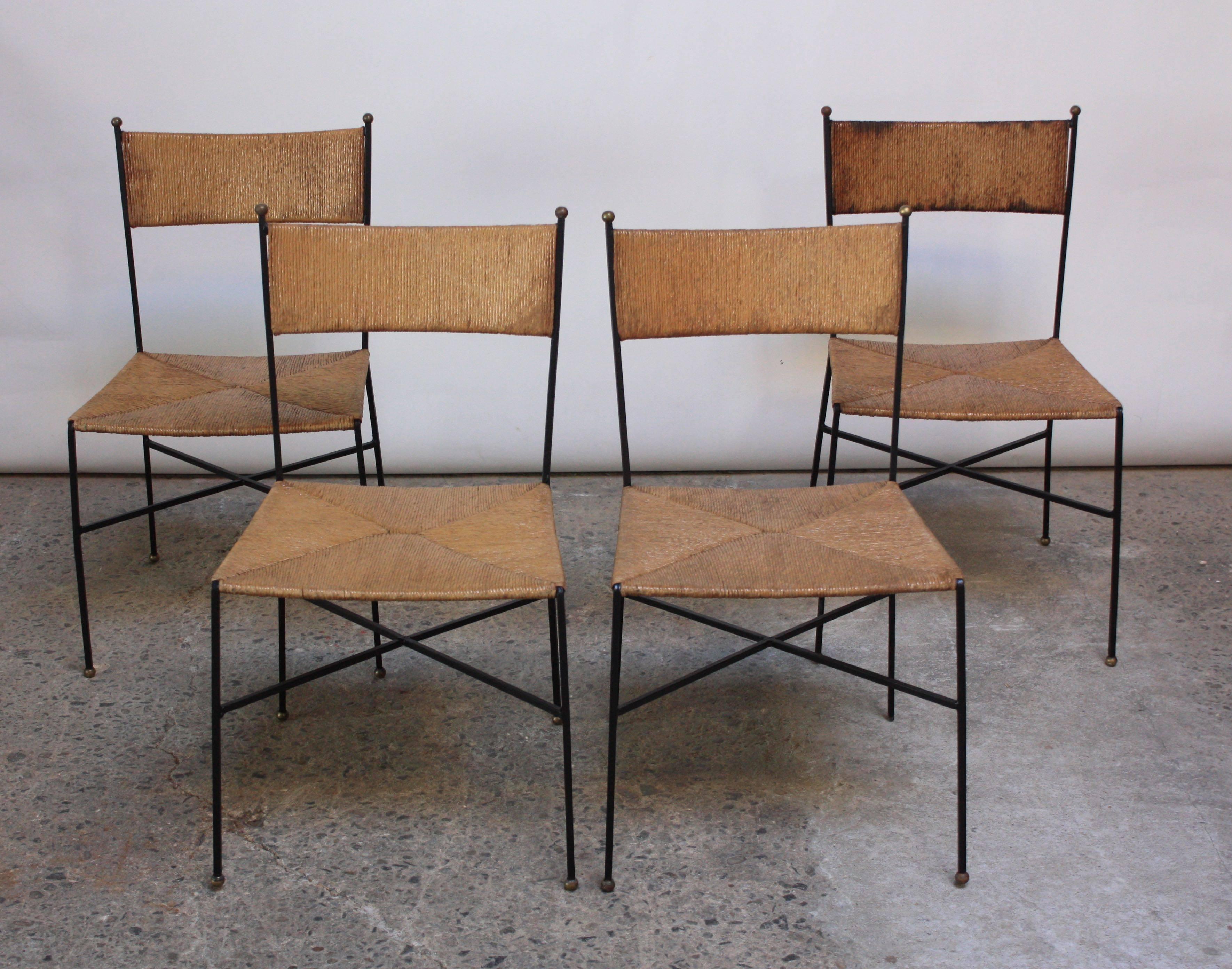 These Milo Baughman chairs were designed in 1954 for Murray Furniture and feature a rush back and set, iron frame, and brass finials (six to a chair). These chairs are uncommon and difficult to find, particularly as a set of four. They are suited