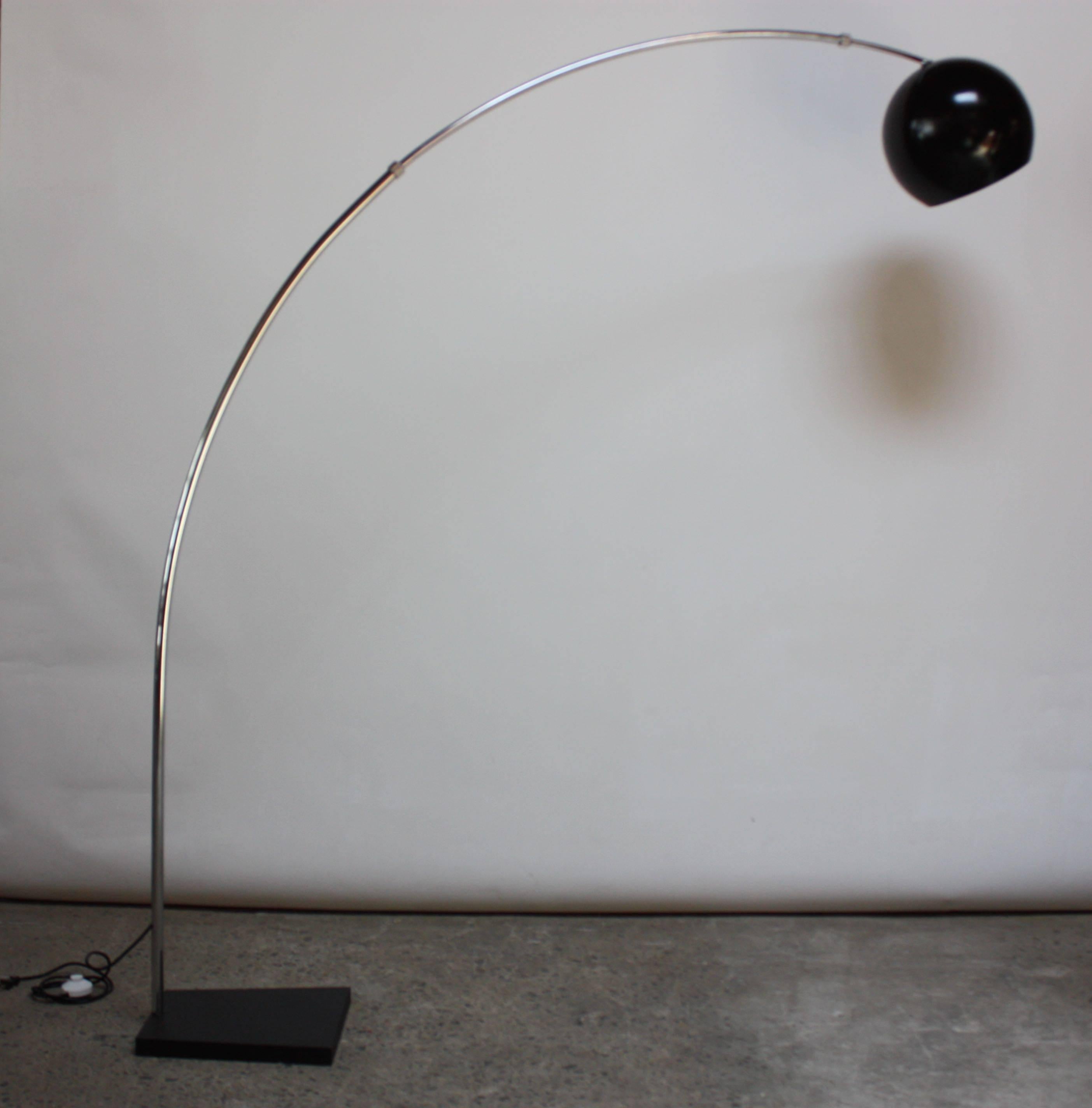 This arching lamp is comprised of an oversized painted black metal shade atop a chromed steel 'arch' and cast steel base. The entire arm pivots full 360 on the a cast steel base. The shade can be lowered to the first bracket (pictured) and or the