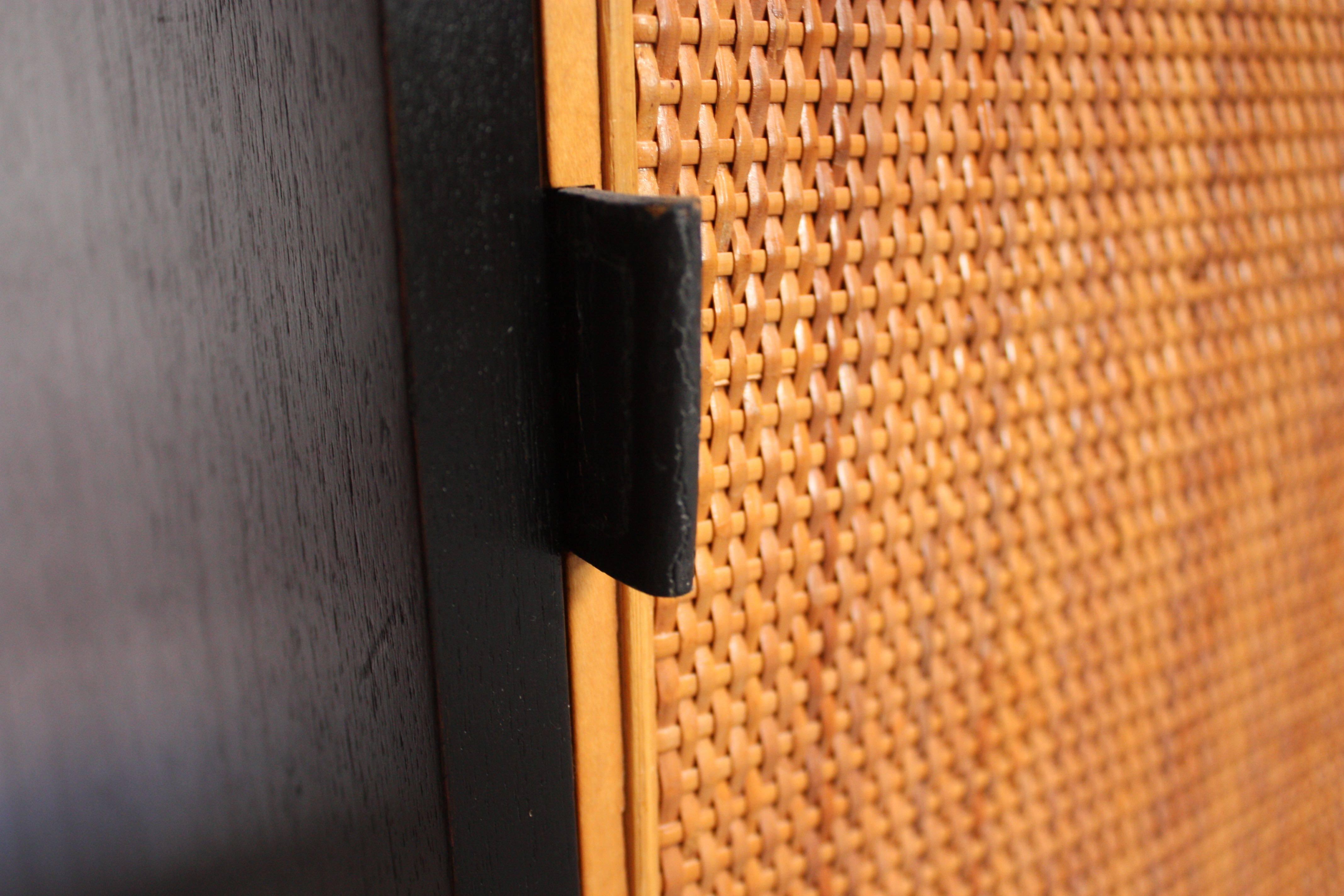 This Florence Knoll ebonized cabinet features two cane-front sliding doors with Knoll's signature hide leather pull tabs concealing one drawer and seven adjustable shelves. The white lacquer interior is original and pristine. The piece sits on