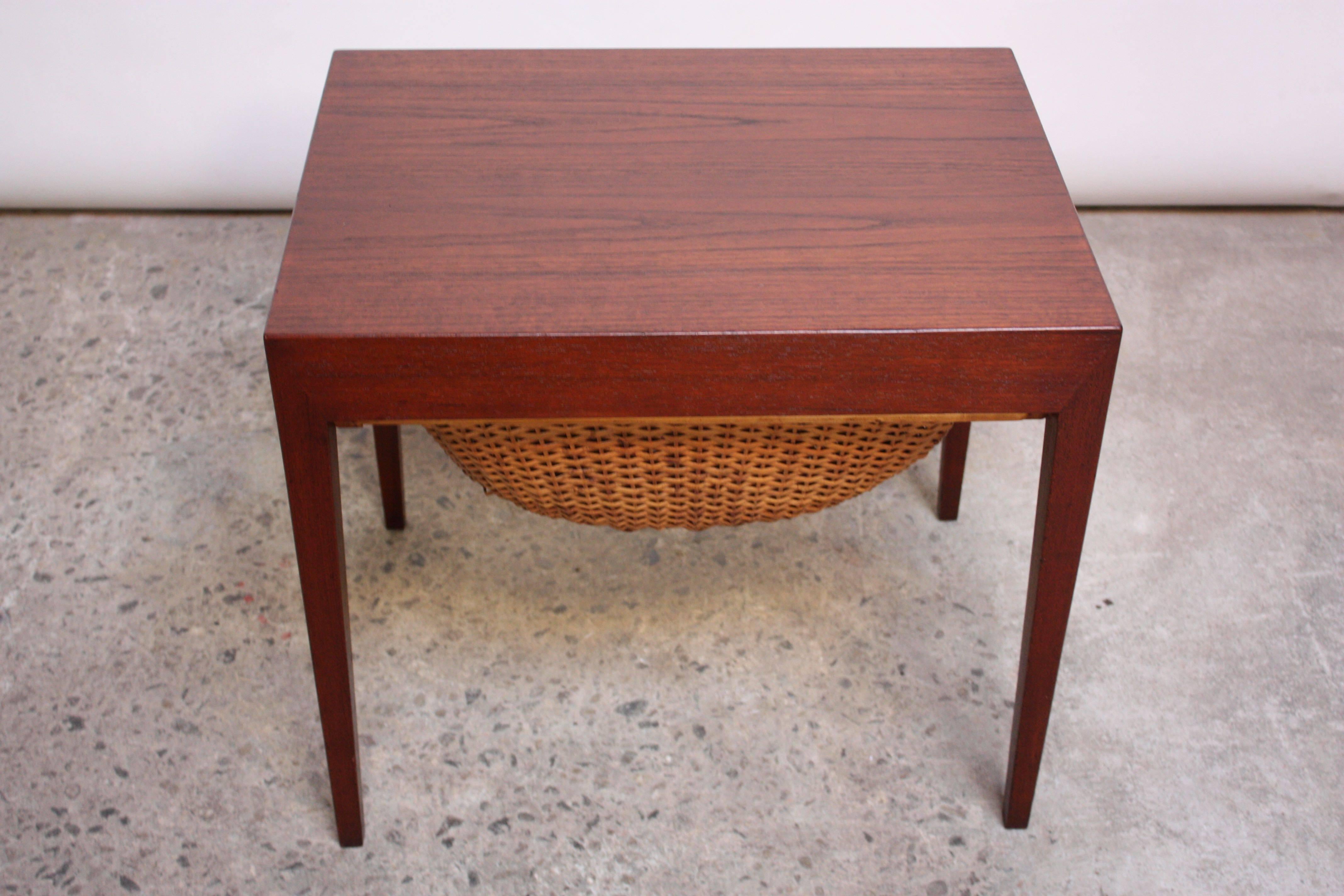 This teak sewing table was designed by Severin Hansen Jr. for Haslev Mobelsnedkeri in the 1960s and is comprised of a woven rattan basket below a shallow, hidden drawer, fitted for sewing implements (including a built-in pin-cushion). Although the