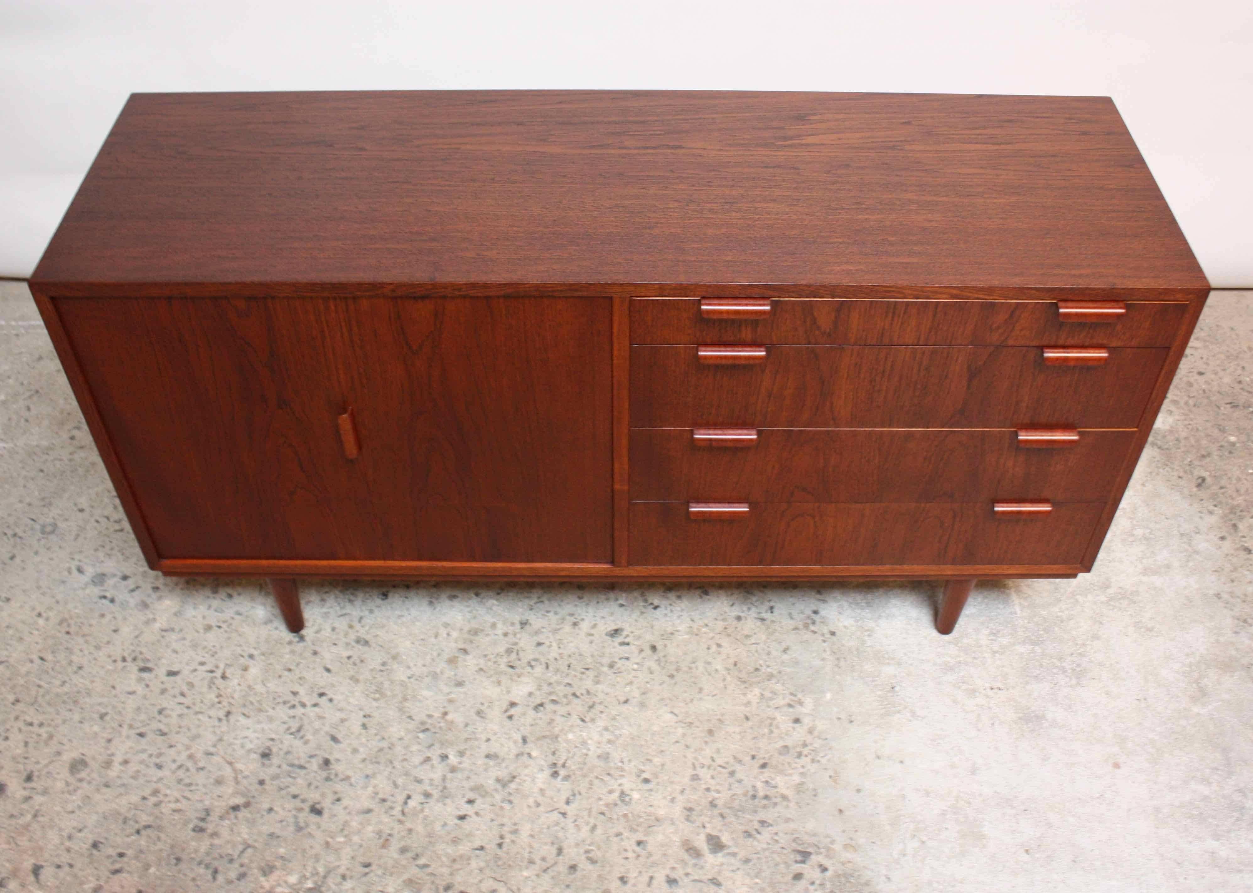 This Danish teak sideboard/cabinet was designed in the 1950s by Carlo Jensen for Poul Hundevad. This small cabinet features a bi-fold door on the left side which opens to reveal a single, adjustable shelf. There are four drawers on the right side