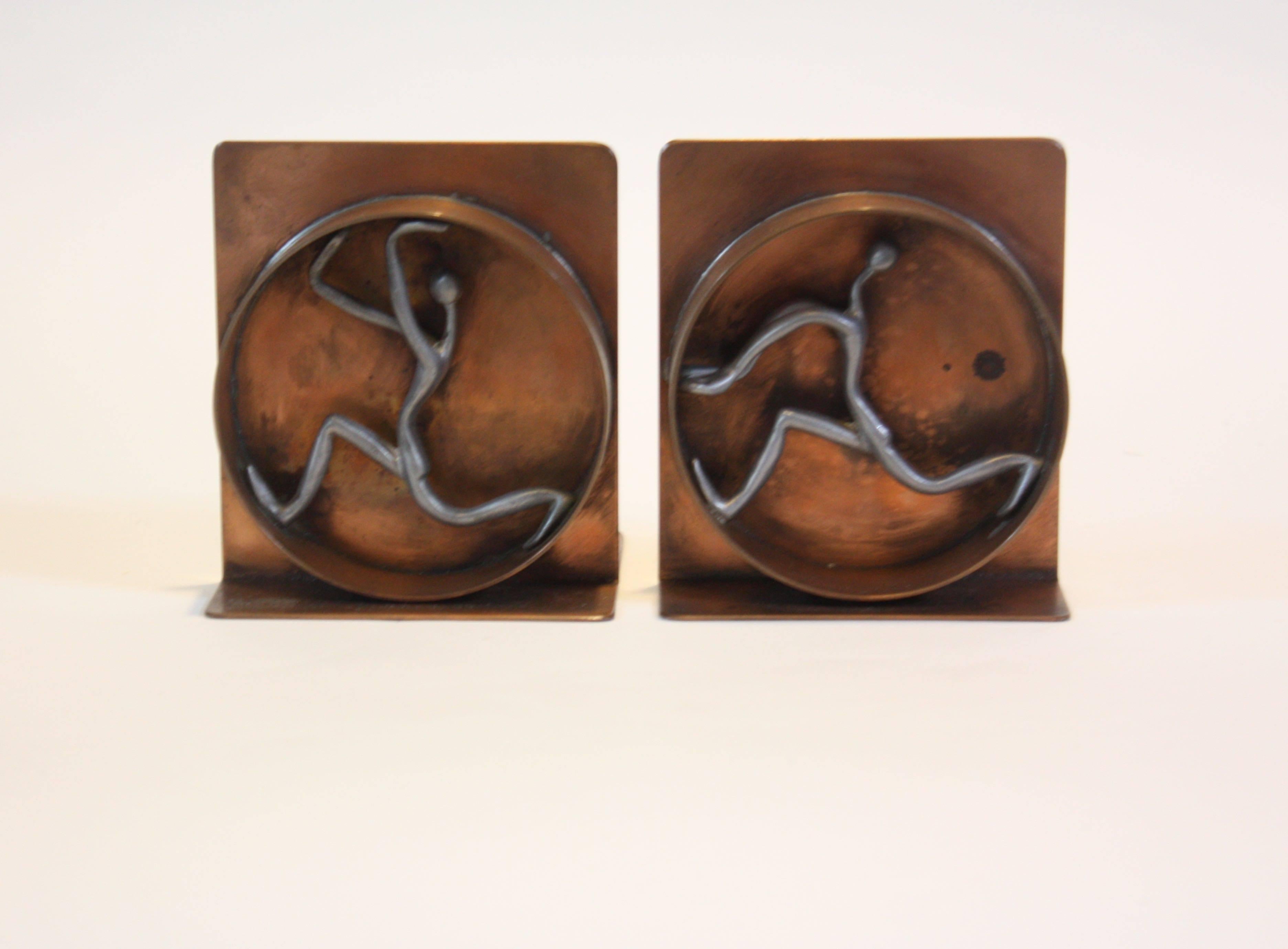 These whimsical bookends depict two human figures running on human hamster wheels. The figures themselves are pewter, and the bookends are copper. Artist signed on both bookends.