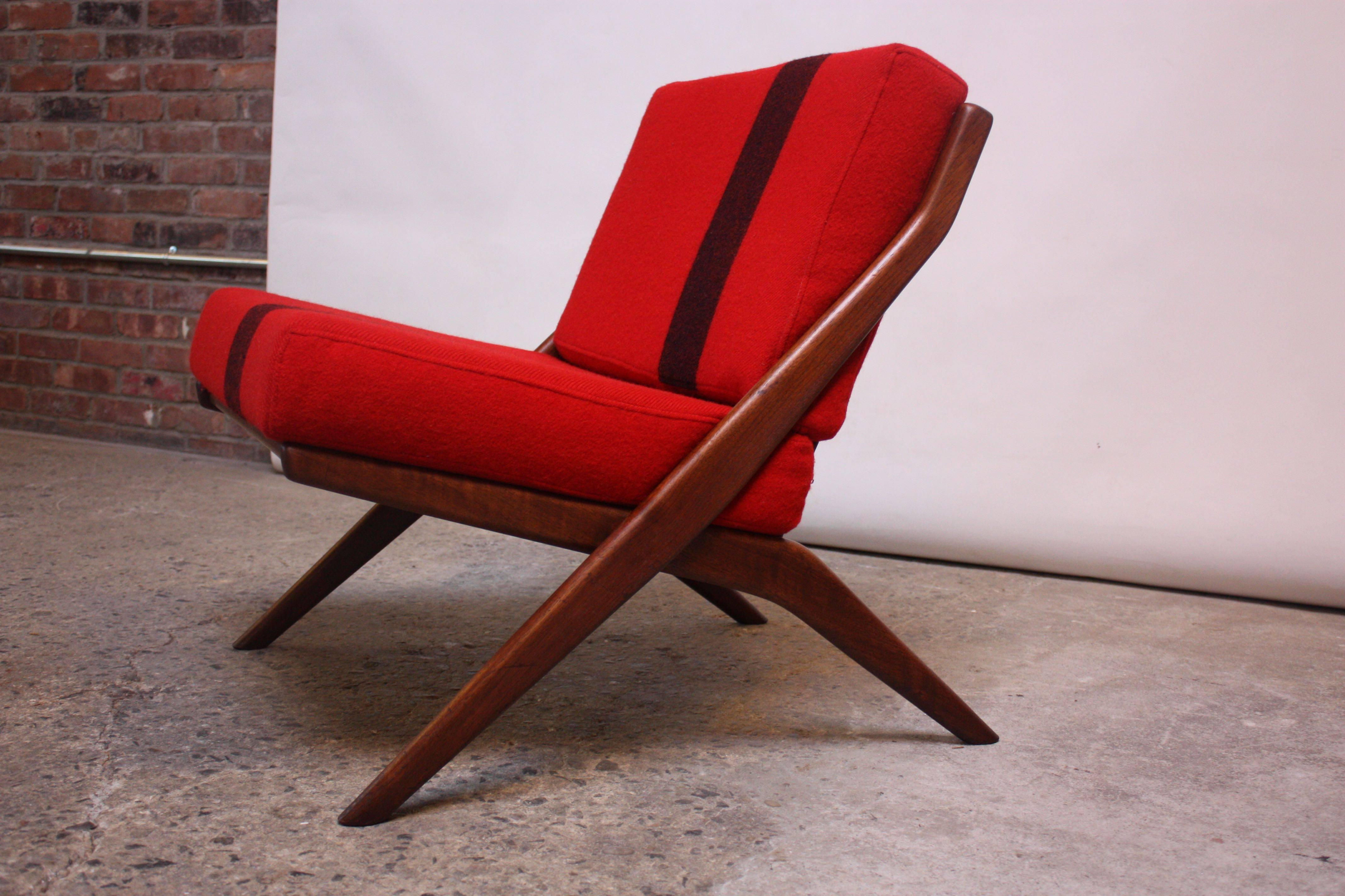 This teak example of Folke Ohlsson's 'Scissor Chair' boasts sculptural, severe lines (best seen from the profile view) contrasted with a simple, Classic slatted back design. 
The straps have been replaced and the cushions have been remade in a