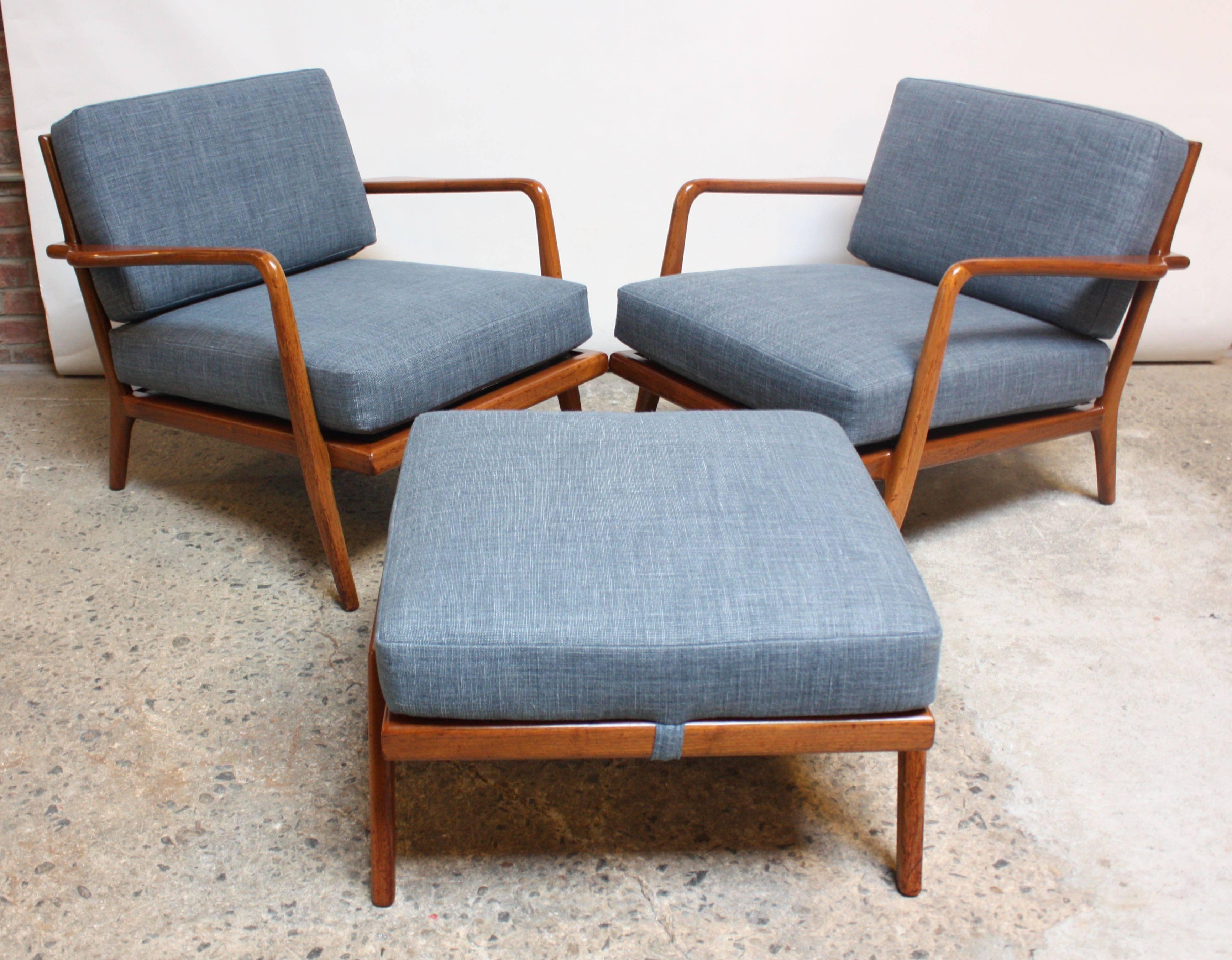 This pair of chairs and single ottoman were designed by Mel Smilow in the 1950s. Solid walnut construction with newly upholstered cushions in a blue linen. The steel straps and metal springs are sound. These extraordinary, vintage examples are