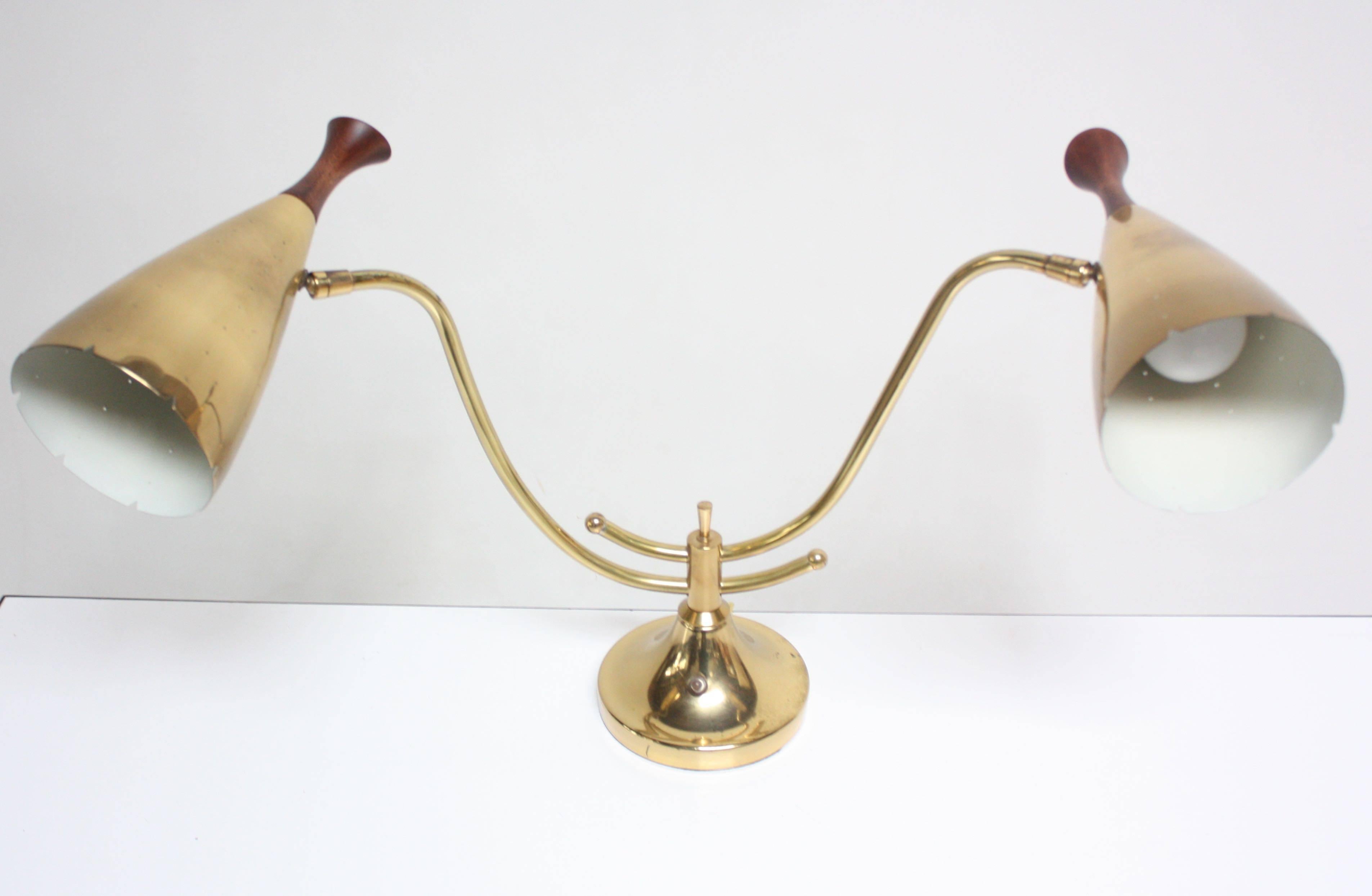 This American modern brass table lamp features two adjustable brass fixtures with sculpted walnut finials (only the fixtures themselves, not the arms, adjust). The perforated brass shade design is reminiscent of Paavo Tynell's designs for Taito Oy.