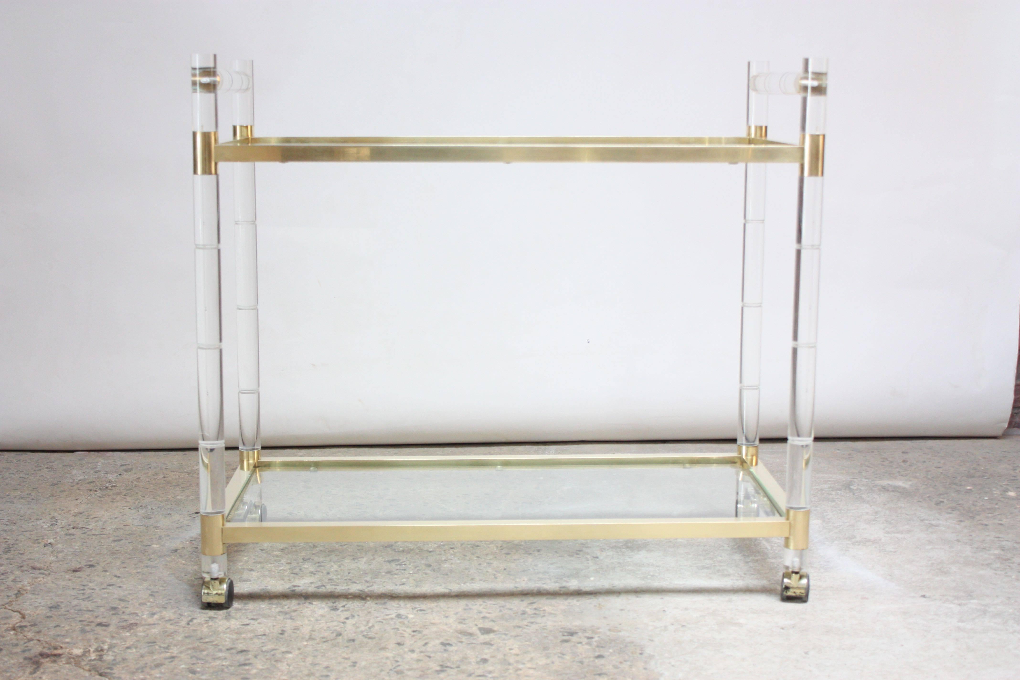 Two-tiered serving or bar cart designed in the 1960s by Charles Hollis Jones for his 'Regency Bamboo' line featuring a brass frame that has been hand-polished to a perfect, satin finish with faux-bamboo lucite rails. The beveled glass surfaces
