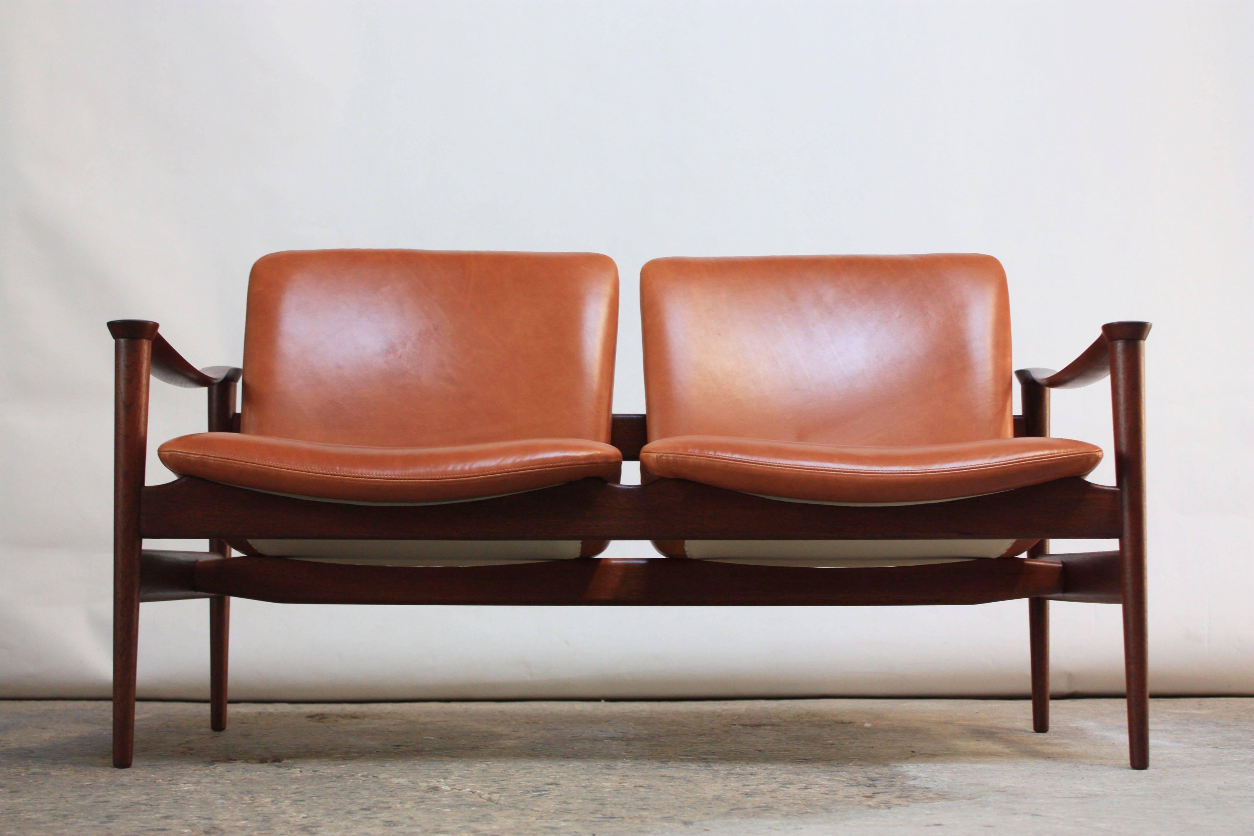 This two-seat sofa was designed by Fredrik Kayser for Vatne Lenestolfabrikk (ca. 1960s, Norway). 
Magnificent frame in sculpted teak with armrests resembling two conjoined cul-de-sacs. 
Solid patinated brass posts connect the seats to the frame in