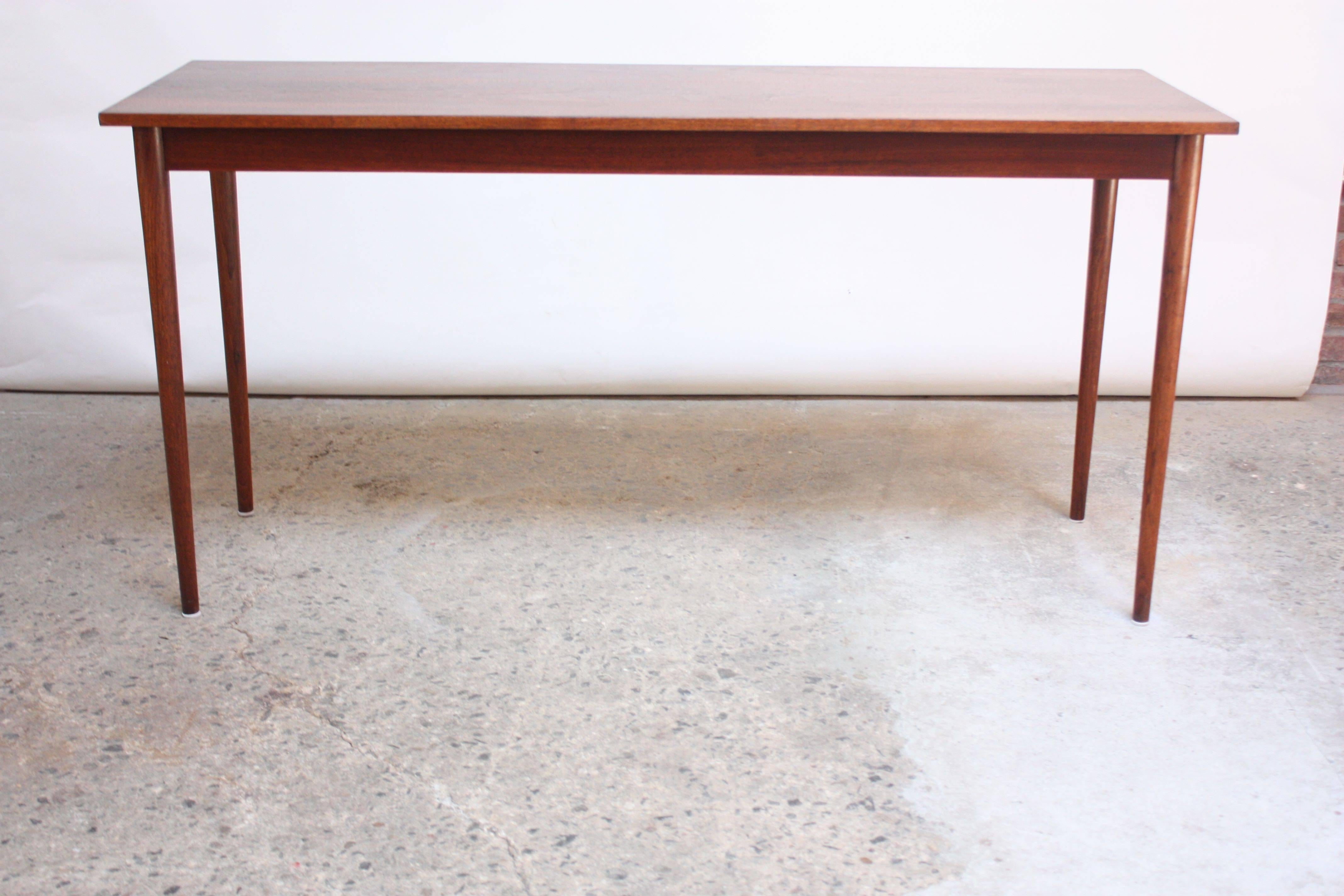 This 1960s sculptural table boasts rich walnut grain, thin, tapered legs and clean lines. Although, the narrowness of this piece makes it an ideal candidate for use as a console table, it can be additionally be used as a desk, entryway table or bar.
