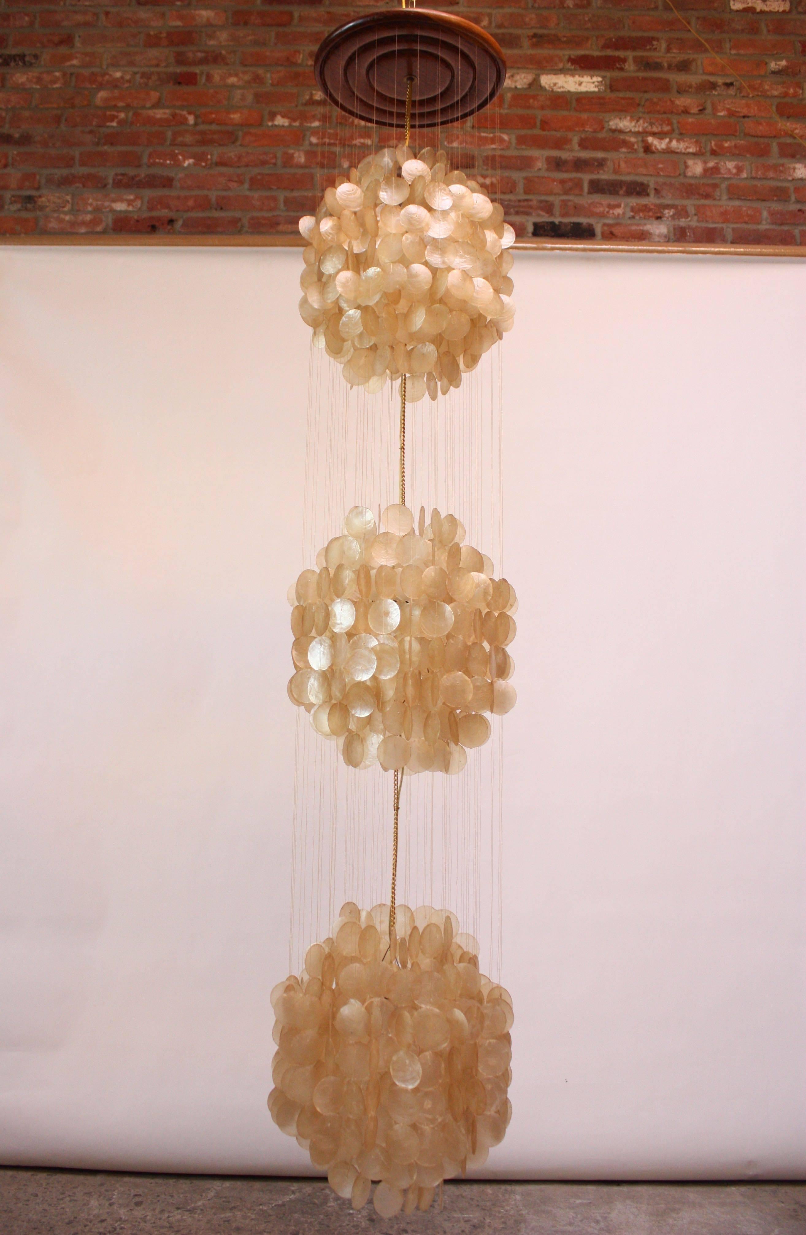 Spectacular three-tiered capiz shell fixture reminiscent of Panton's 1964 '3DM' design. Composed of nylon thread connecting the capiz shells to the top circular wood mount. Cord runs down the middle of the fixture, and each cluster of shells has its