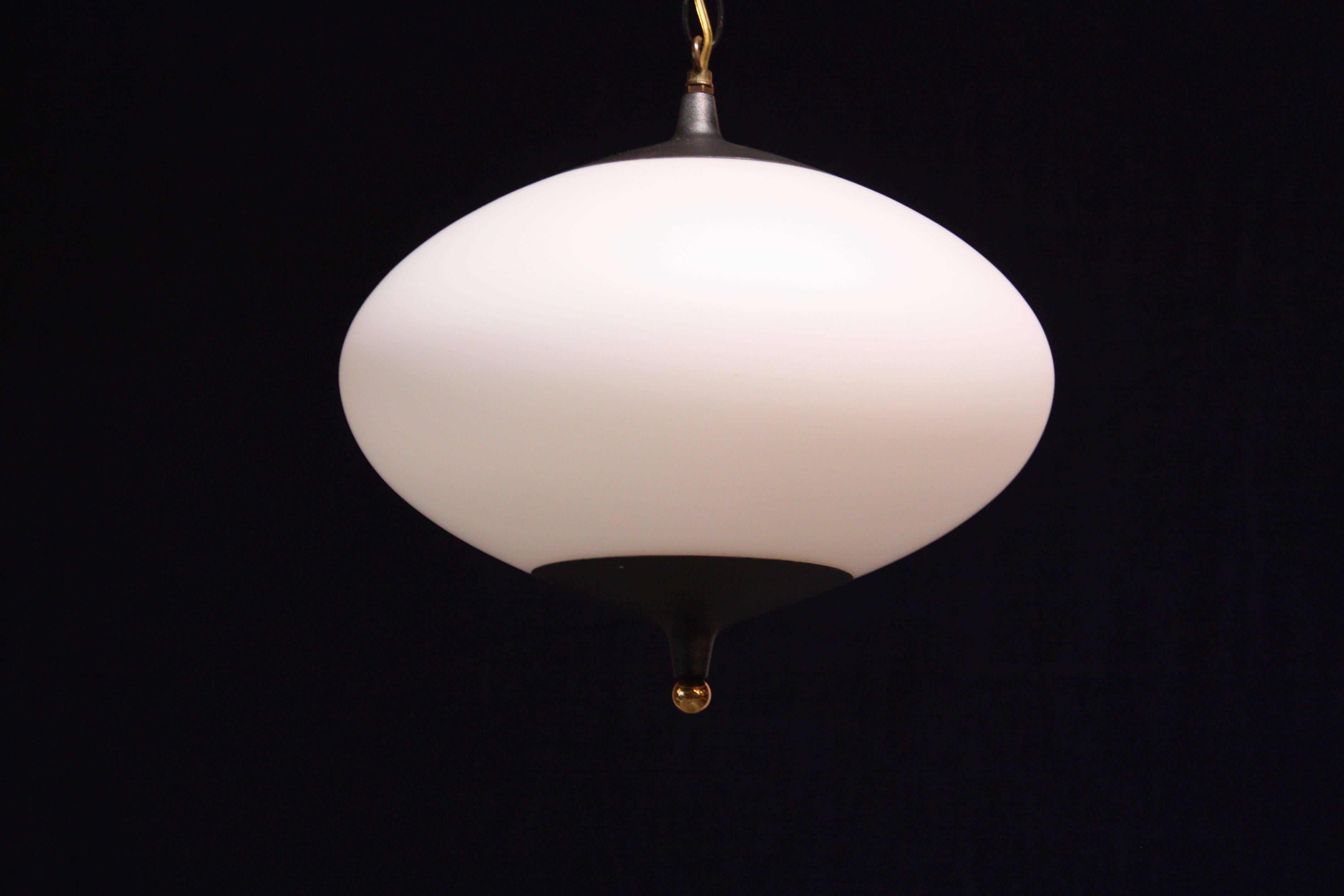 1950s American modern pendant in opal glass with black metal accents and bottom brass finial. The translucent, frosted glass allows for uniform distribution of the light. A powerful light source for a modestly sized fixture.