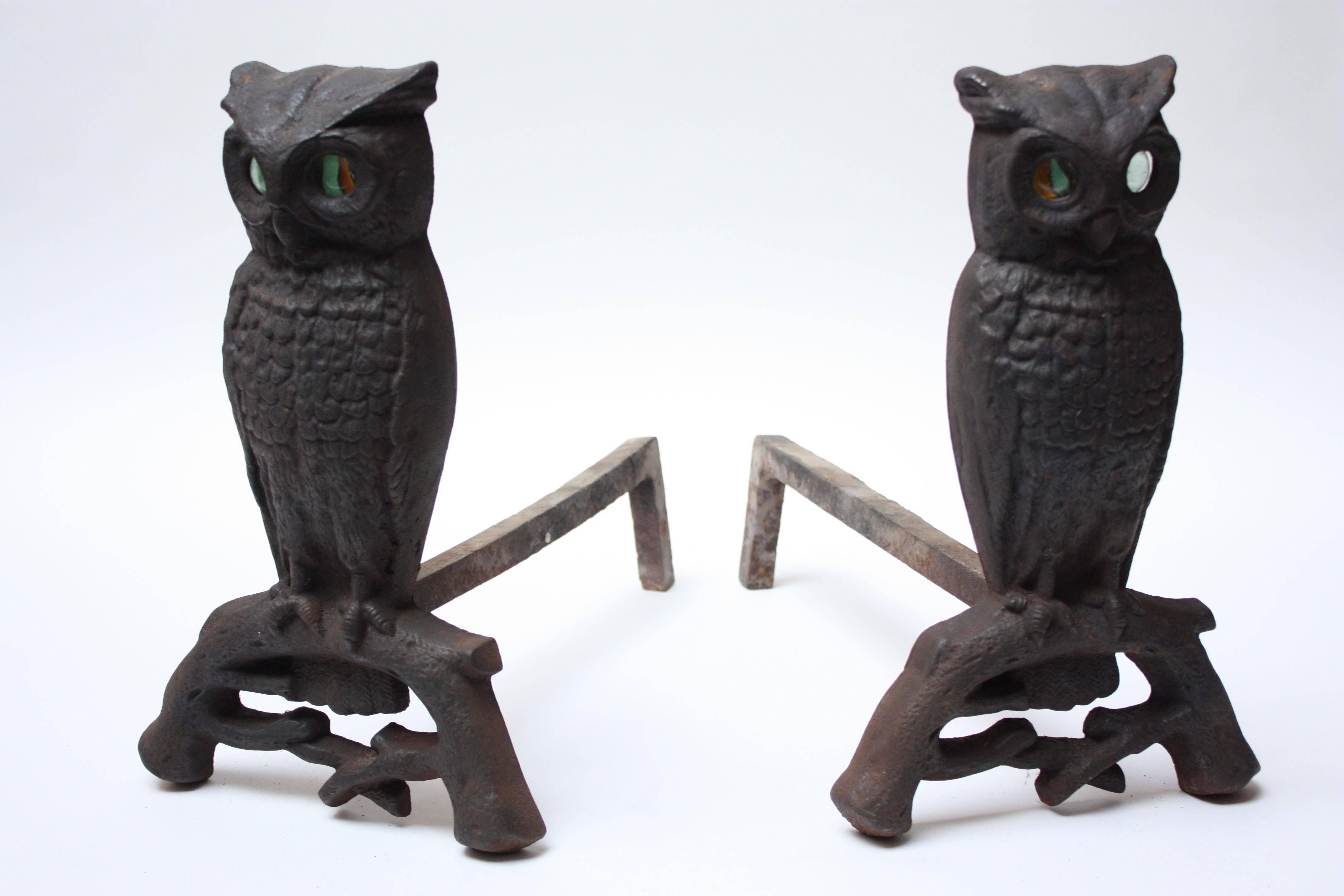 This pair of andirons (circa 1930s) is composed of cast iron owls on arched branch uprights fitted to billet bars. The glass marble eyes are nicely contrasted by the cast iron. All the hardware and parts (screws, glass eyes, etc.) are original; no