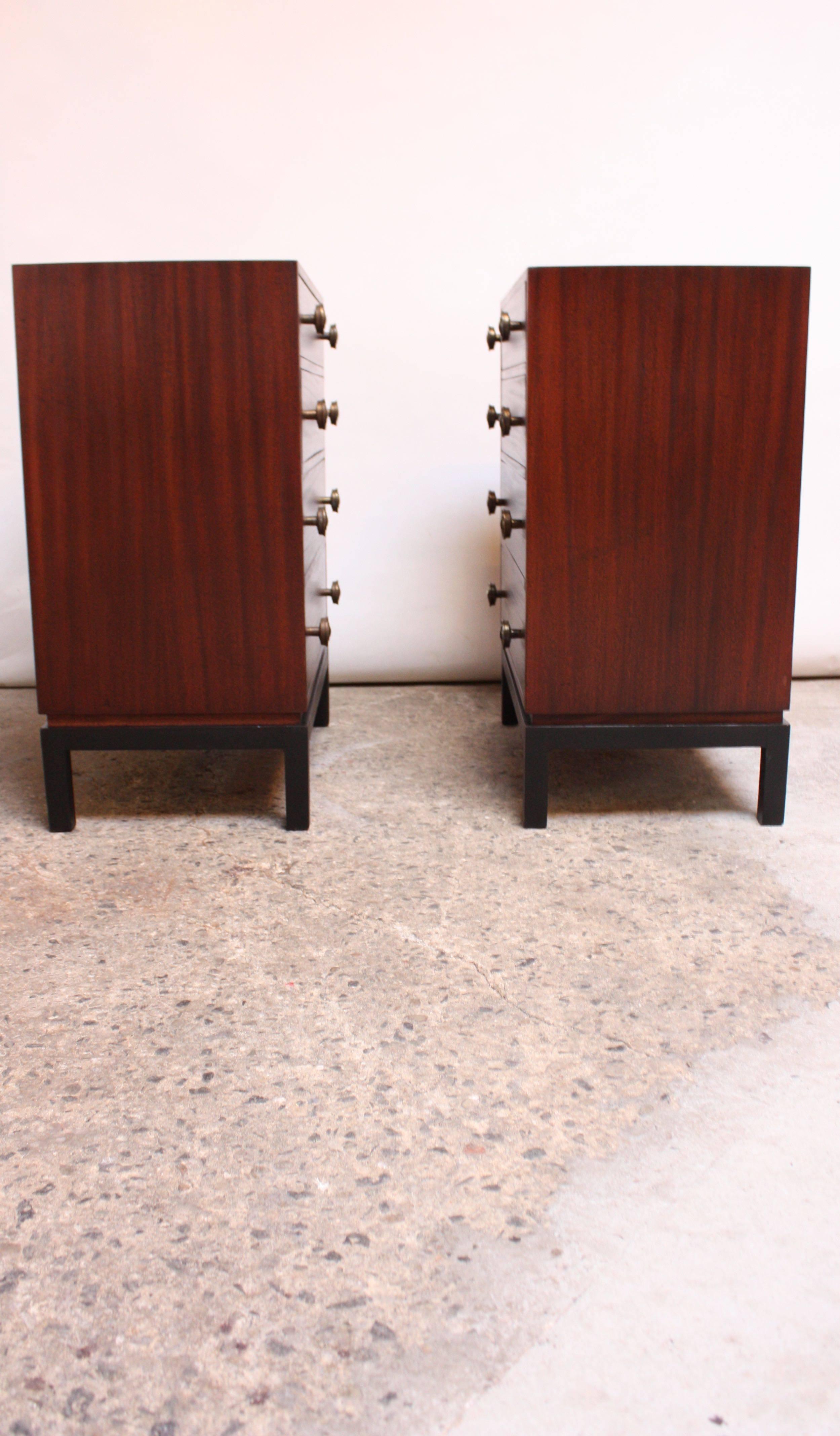 Pair of compact stained mahogany four-drawer chests with ebonized bases and circular, brass pulls. Minimal form is enhanced by the vibrant mahogany grain and ornate detail of the brass accents. Expertly restored, but wear commensurate with age and