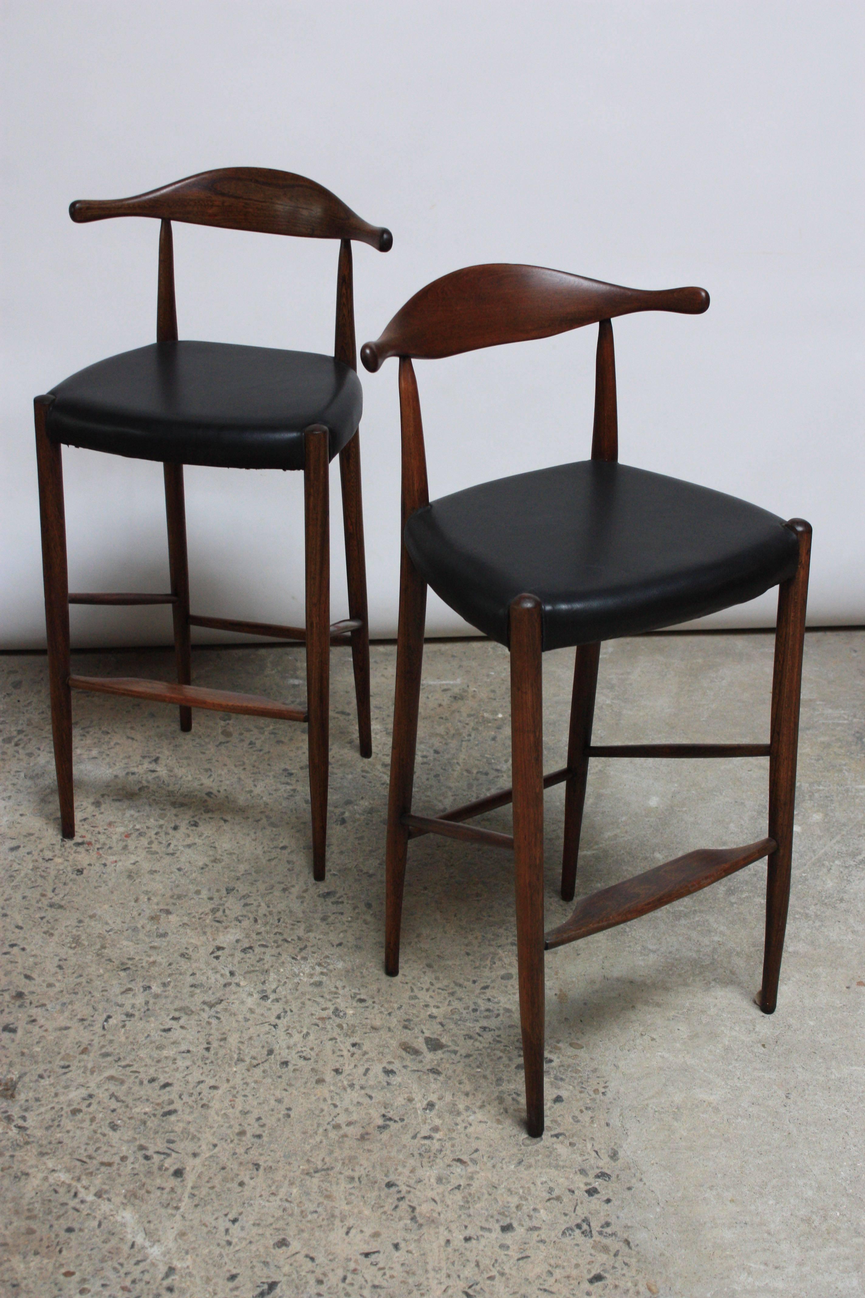 This sculptural pair of Wegner-Style Danish 'cow horn' bar stools is comprised of a black leather seat and teak frame anchored by a hand-carved cow horn back rest.