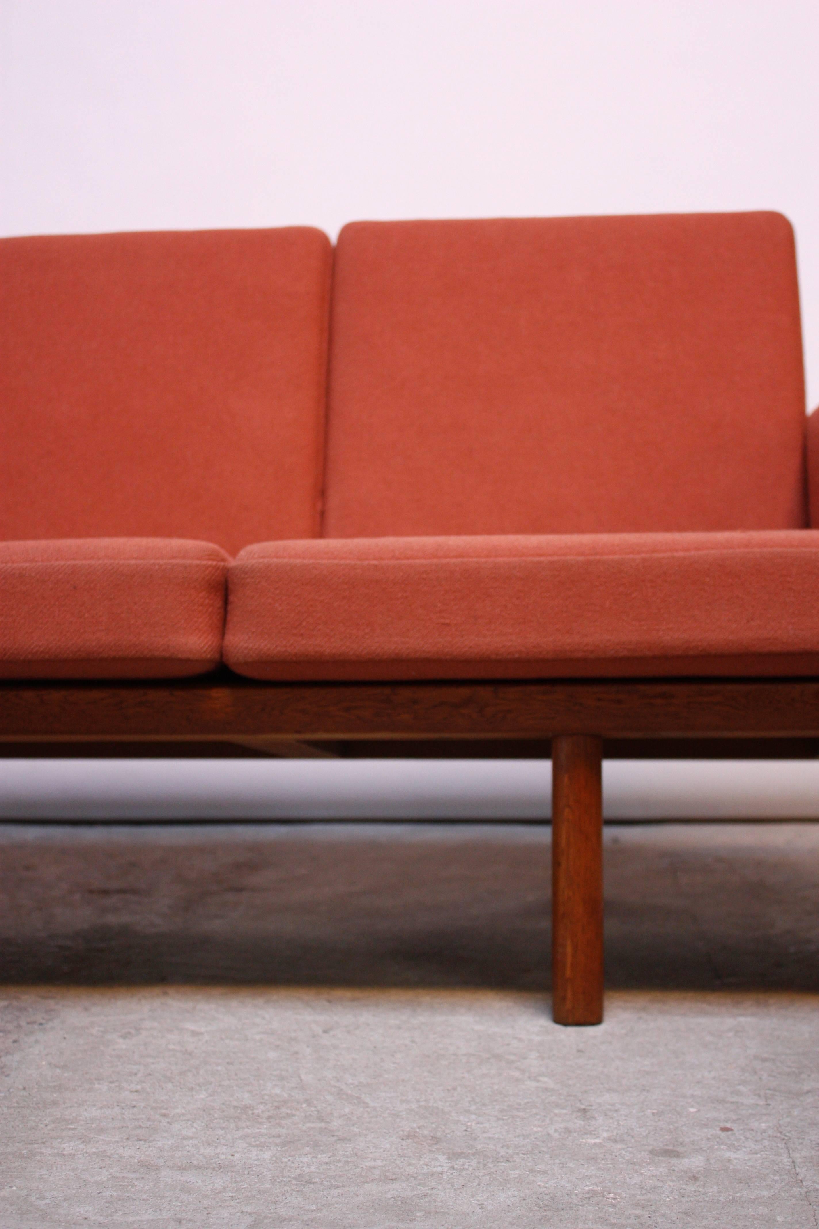 This four-seater sofa (model GE 236/4) was designed by Hans Wegner for GETAMA in the 1950s and is comprised of a solid oak slatted-back frame. The cushions, marked 'Ryghynde' are original to the piece and are a coral/peach wool. The GETAMA branding