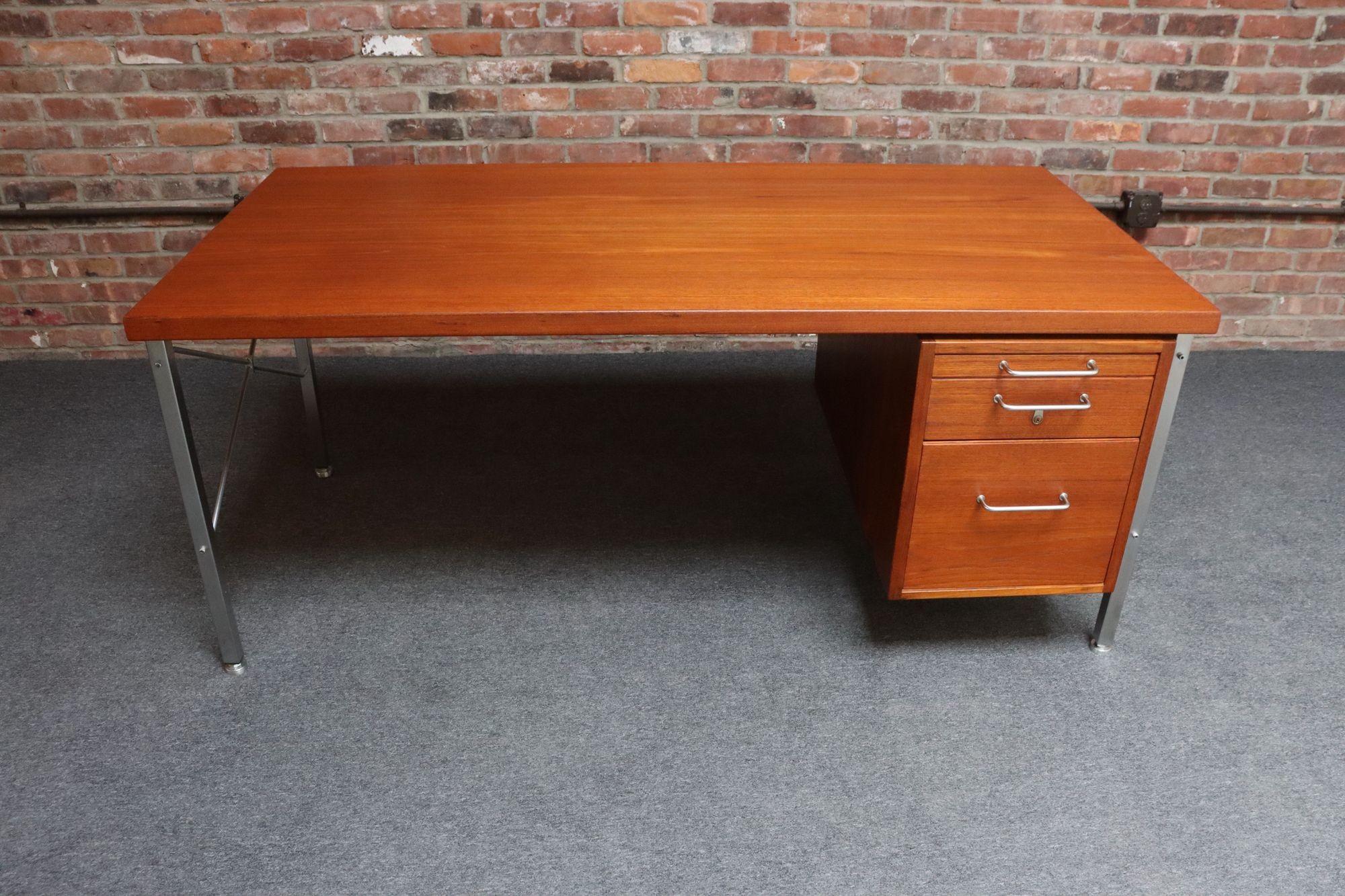 Scrivania direzionale moderna di metà secolo (Kontour - Model A 164 ) di Hans Wegner per Johannes Hansen, 1965 circa, Danimarca.
È composta da una struttura in acciaio inossidabile che sostiene una superficie in teak massiccio e da un banco di tre