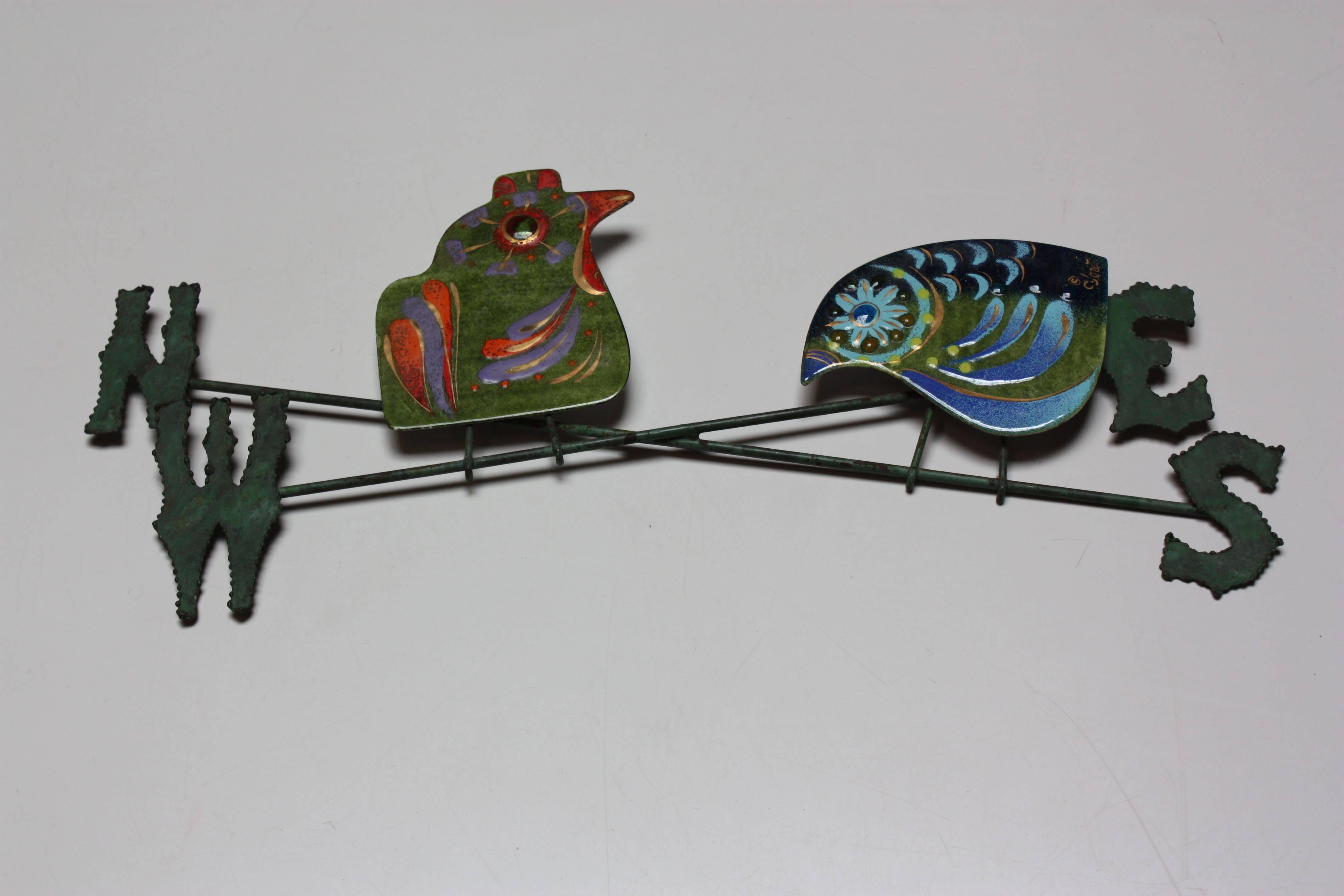 This 1960s Curtis Jere wall sculpture features two vibrant enamel on copper birds atop a verdigris metal weather vane. There is nice age to the rods and some wear (namely a small bend to the bottom left corner of the 'W,' which is barely