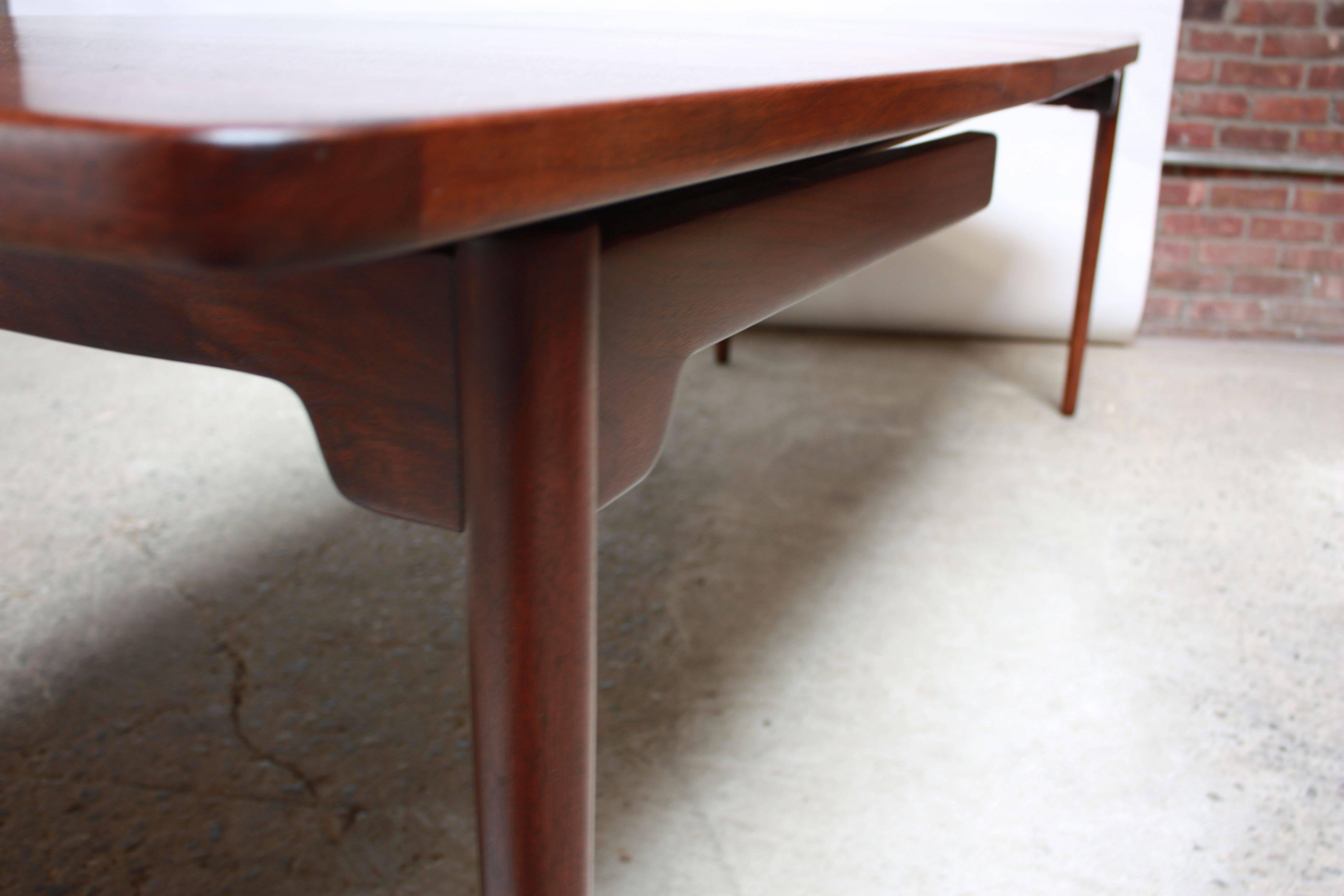 This elegant Jens Risom dining table features a 'floating' walnut surface atop a sculptural base with tapered legs. Designed in the 1950s, this piece was among his earliest designs exhibiting both form and function. The table includes the two