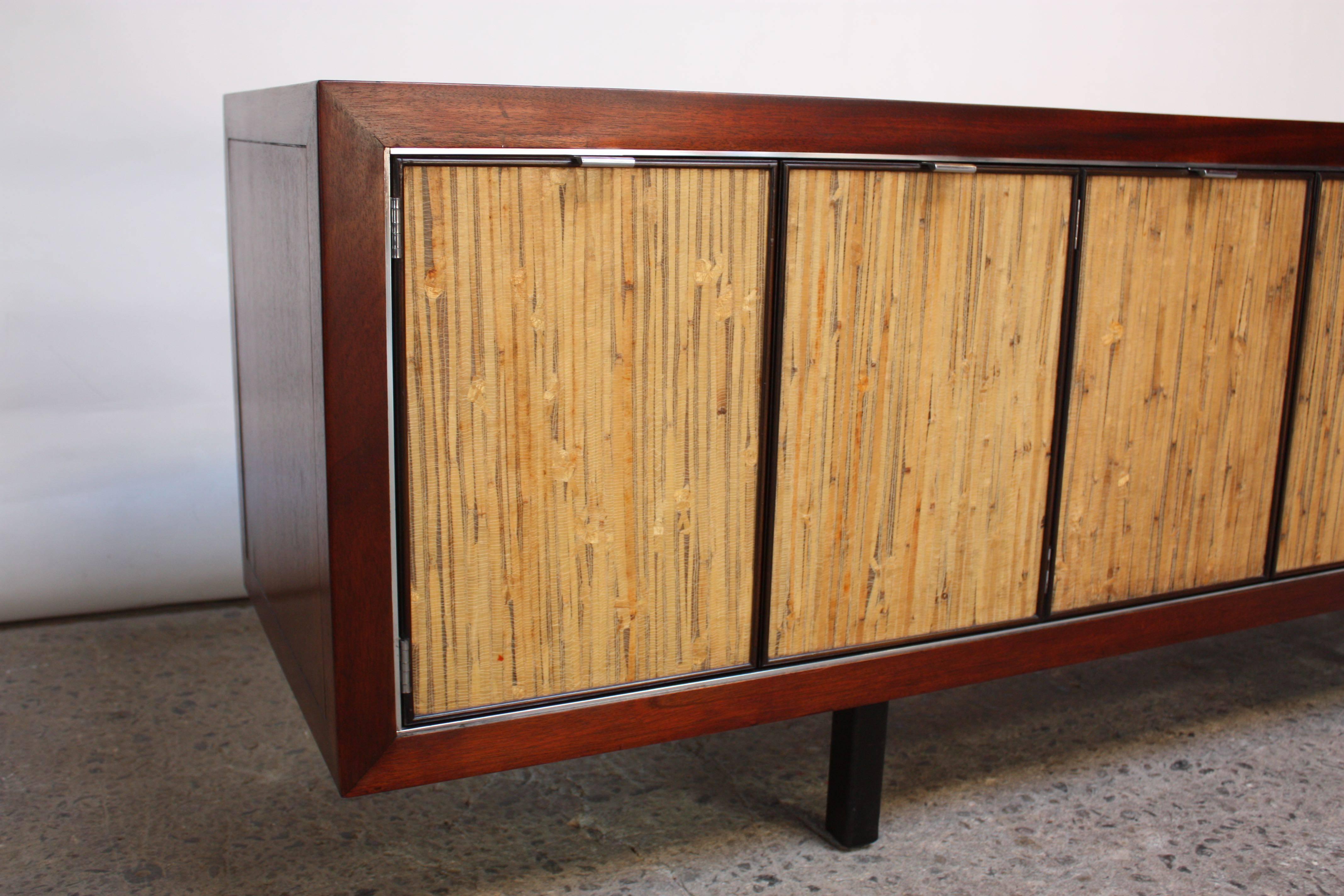This unique credenza features inlaid bamboo panels on the front on which a clear cast resin has been applied for preservation. The cabinet itself is stained walnut contrasted by a cherry trim and incised with an enamel ebony paint. There are three
