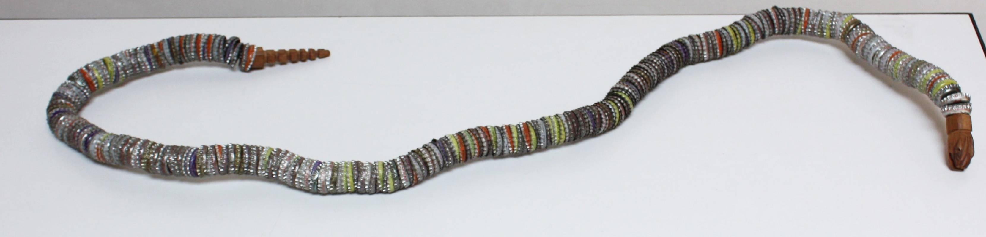 This Felipe Archuleta-style folk art snake is comprised of bottlecaps, a carved wood head and rattle, wire and adhesive. The piece is not painted; the artist employed caps in lime green, orange and blue (among others) to give the body a natural