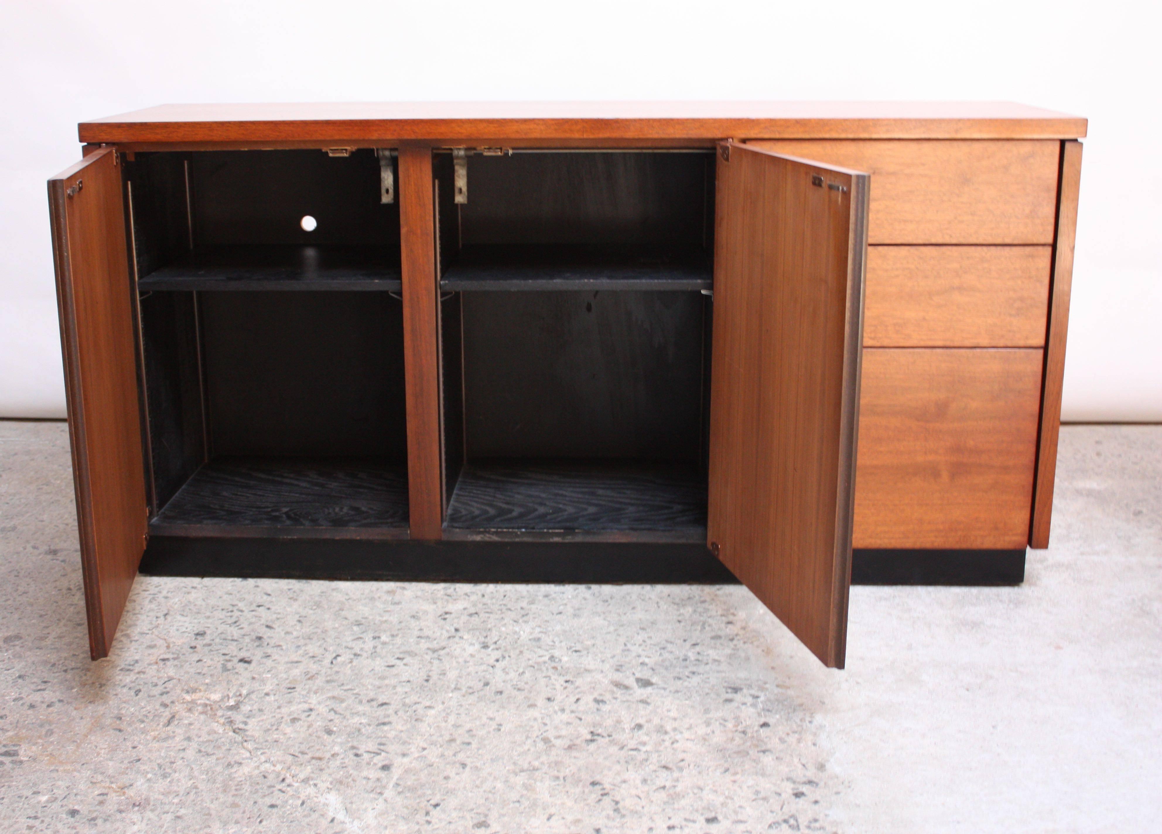 This walnut cabinet was manufactured by Lehigh Leopold in the 1970s and is comprised of two doors which open to reveal removable / adjustable shelves (a total of two). There are three drawers to the right for additional storage. The ebonized oak