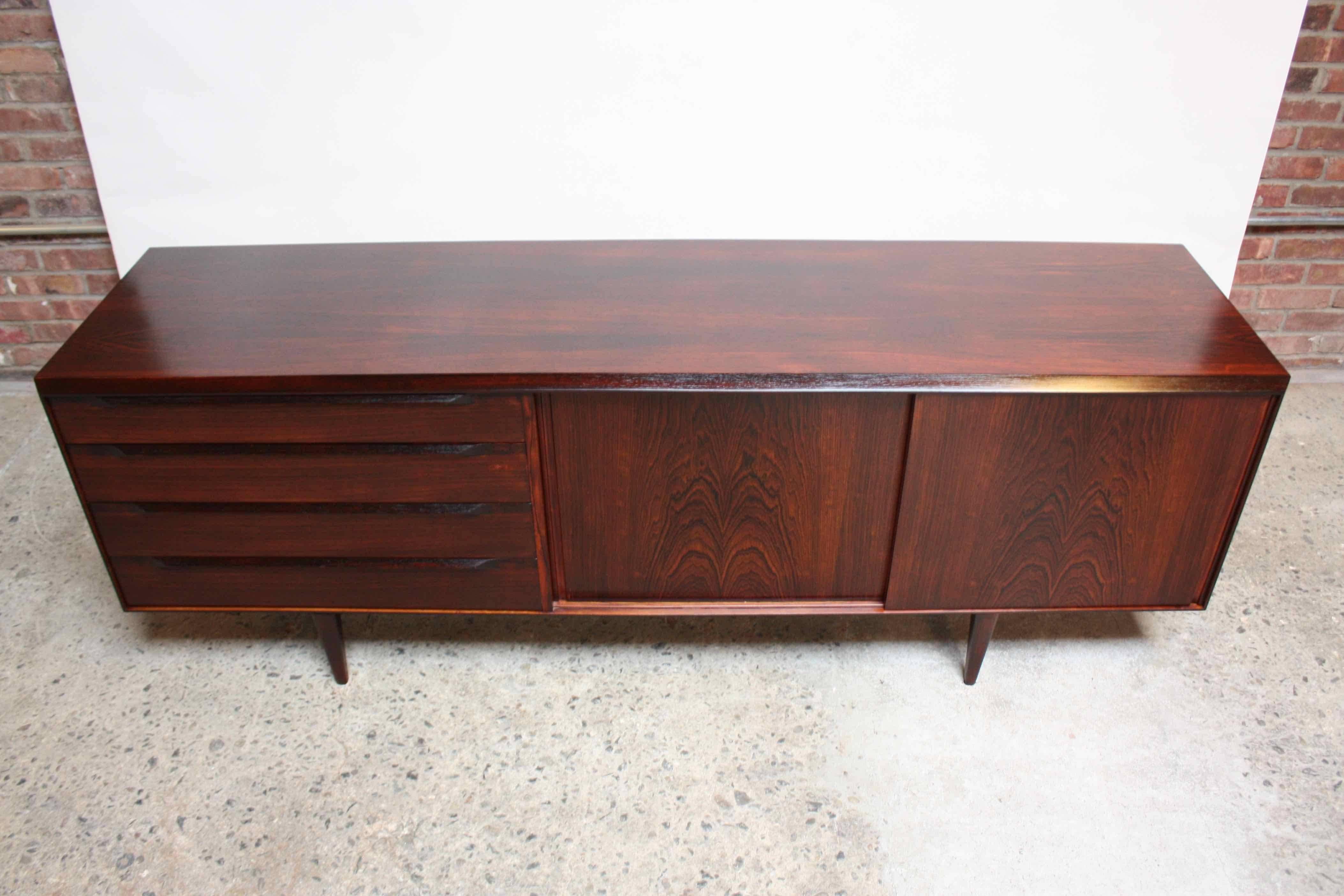This exceptional low and sleek rosewood sideboard was designed by Kai Kristiansen in the 1960s. 
The bookmatched sliding doors open to reveal two adjustable shelves (one/side.) There are four drawers on the other side for additional storage.