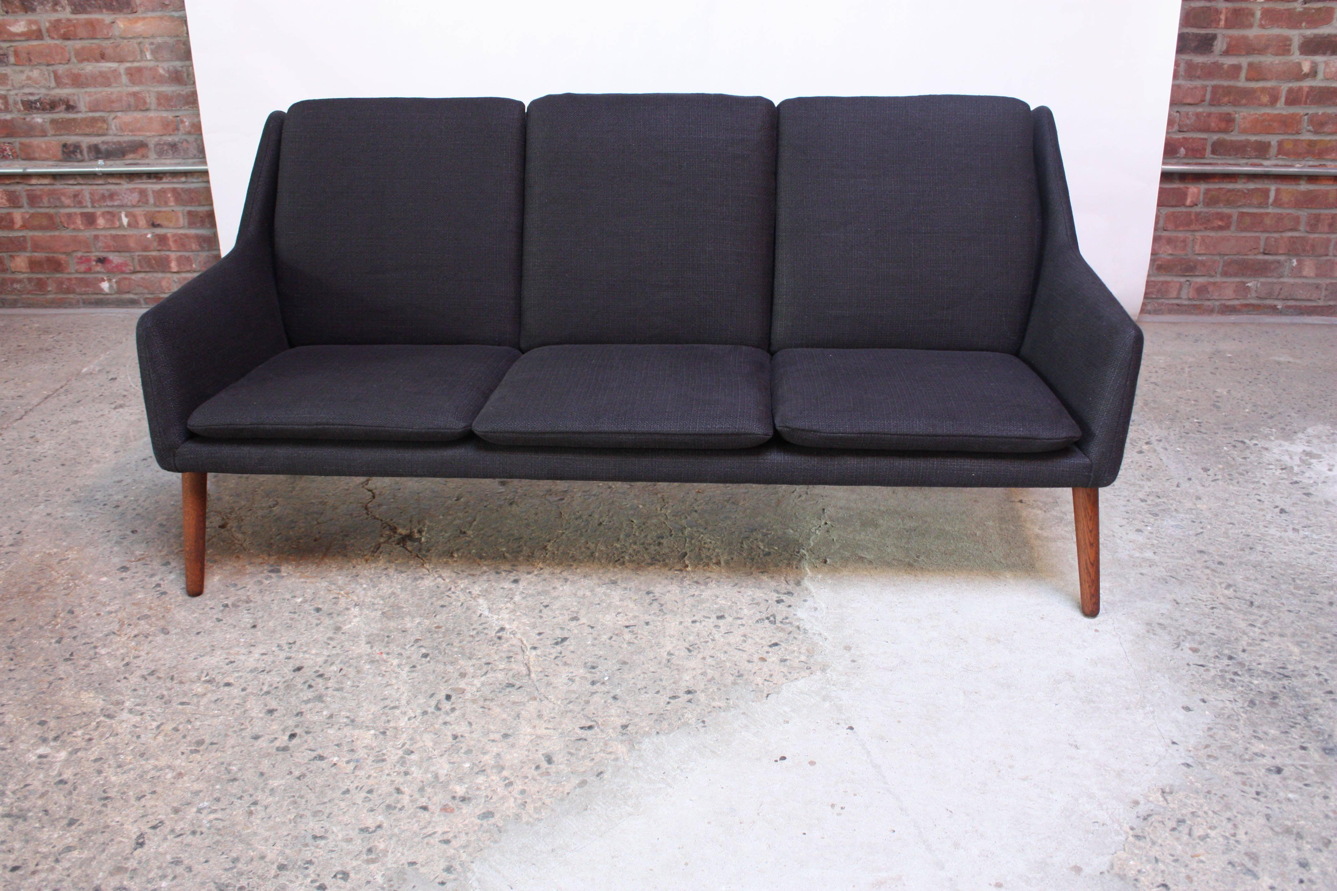 This rarely seen Danish Sofa was designed by Erik Osterman and H. Høpner Petersen for Godtfred Petersen in the late 1950s. It boasts clean lines, accentuated by thin, stained-oak splayed legs. The solid black tweed upholstery is new and the foam has