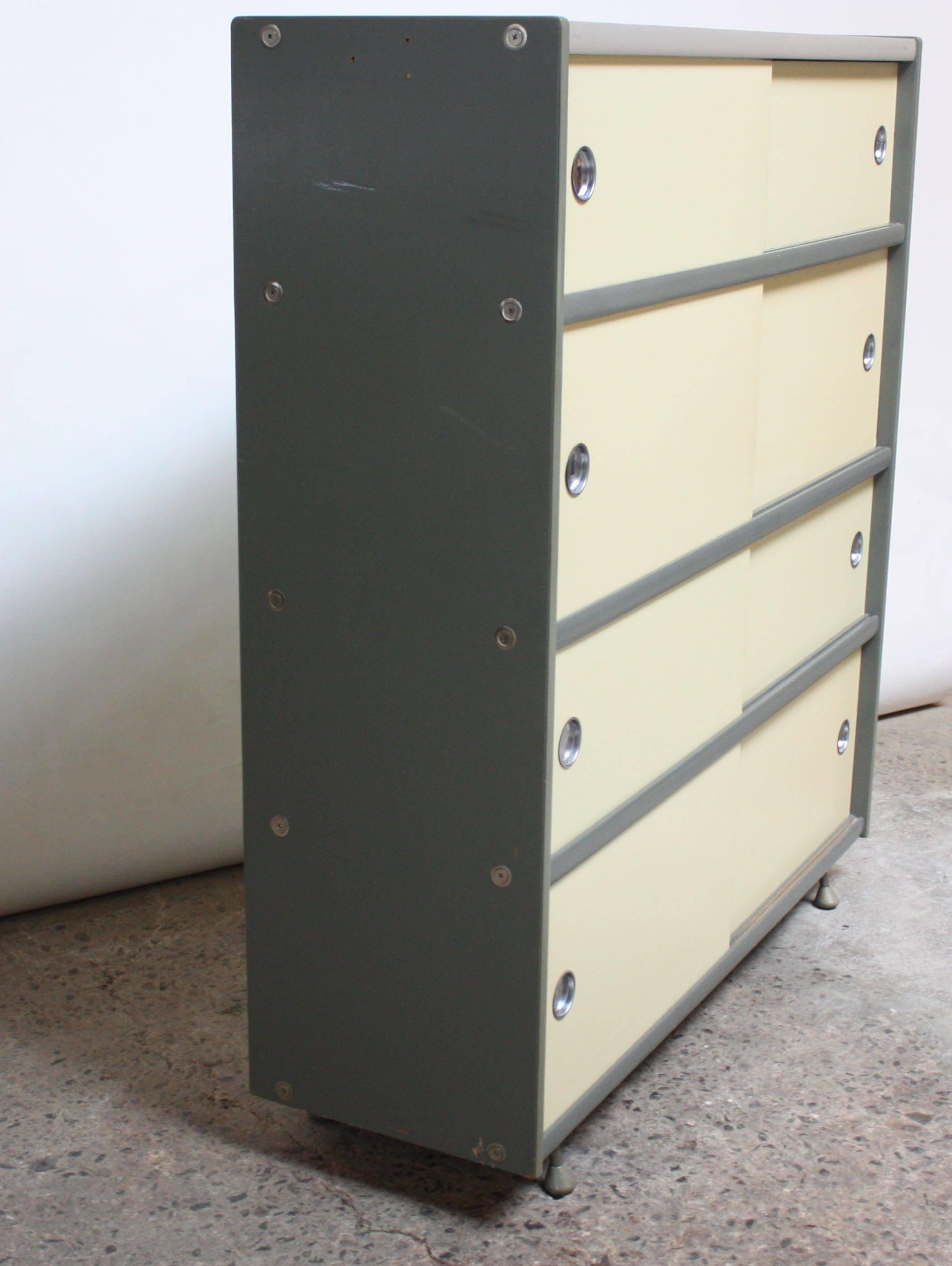 This Bauhaus-style storage cabinet is a rare example from Brunswick, scarcely seen in its original finish. Although it is often attributed to Raymond Loewy, Bill Renwick actually designed this unit in the 1950s. It is composed of a painted gray