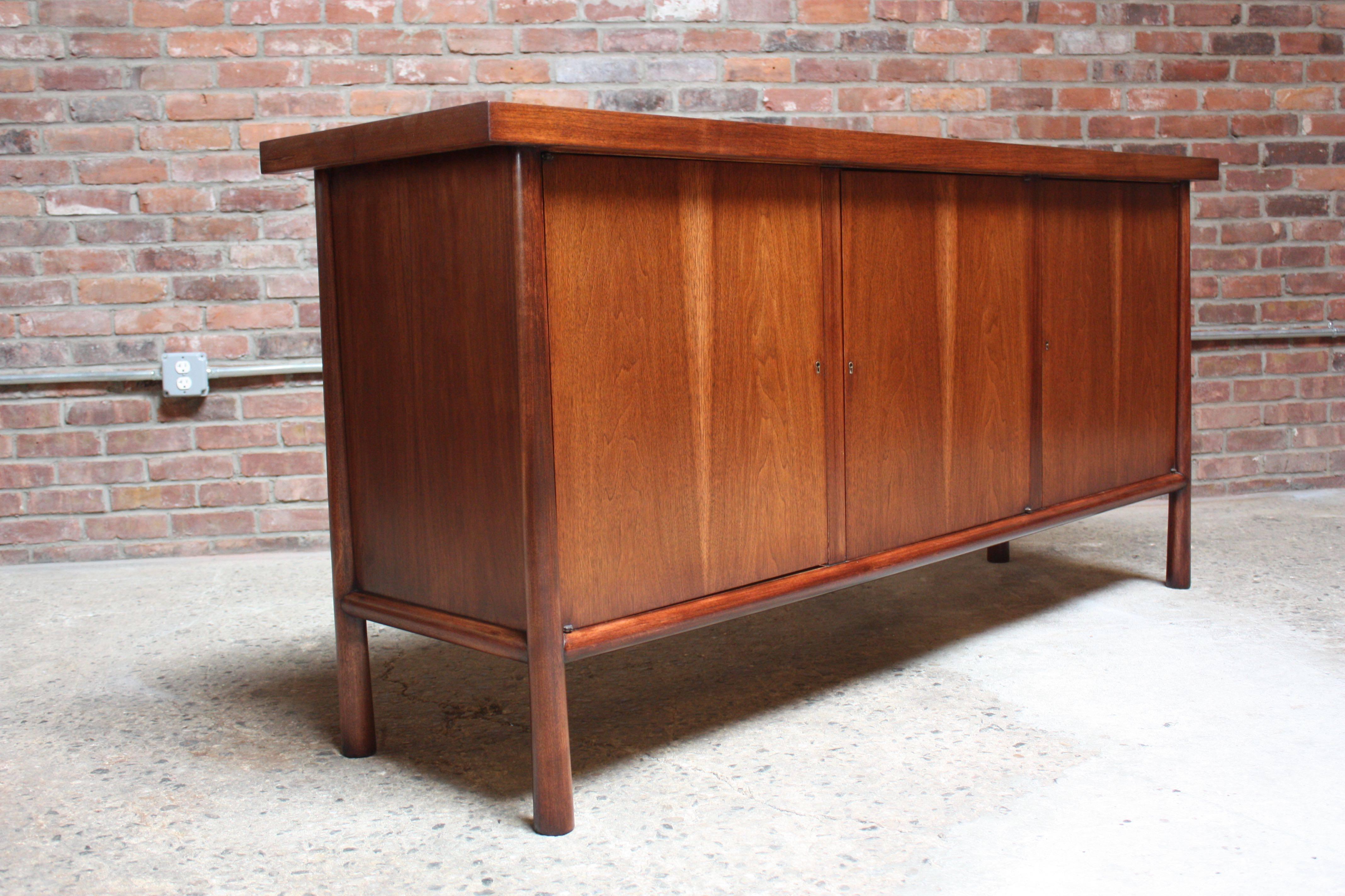 Exquisite and uncommon walnut three door-cabinet with oversized surface and sculptural, tapered legs designed by Robsjohn-Gibbings for Widdicomb in the 1950s. The left and right cabinet doors open to reveal adjustable shelves (one / side), and the