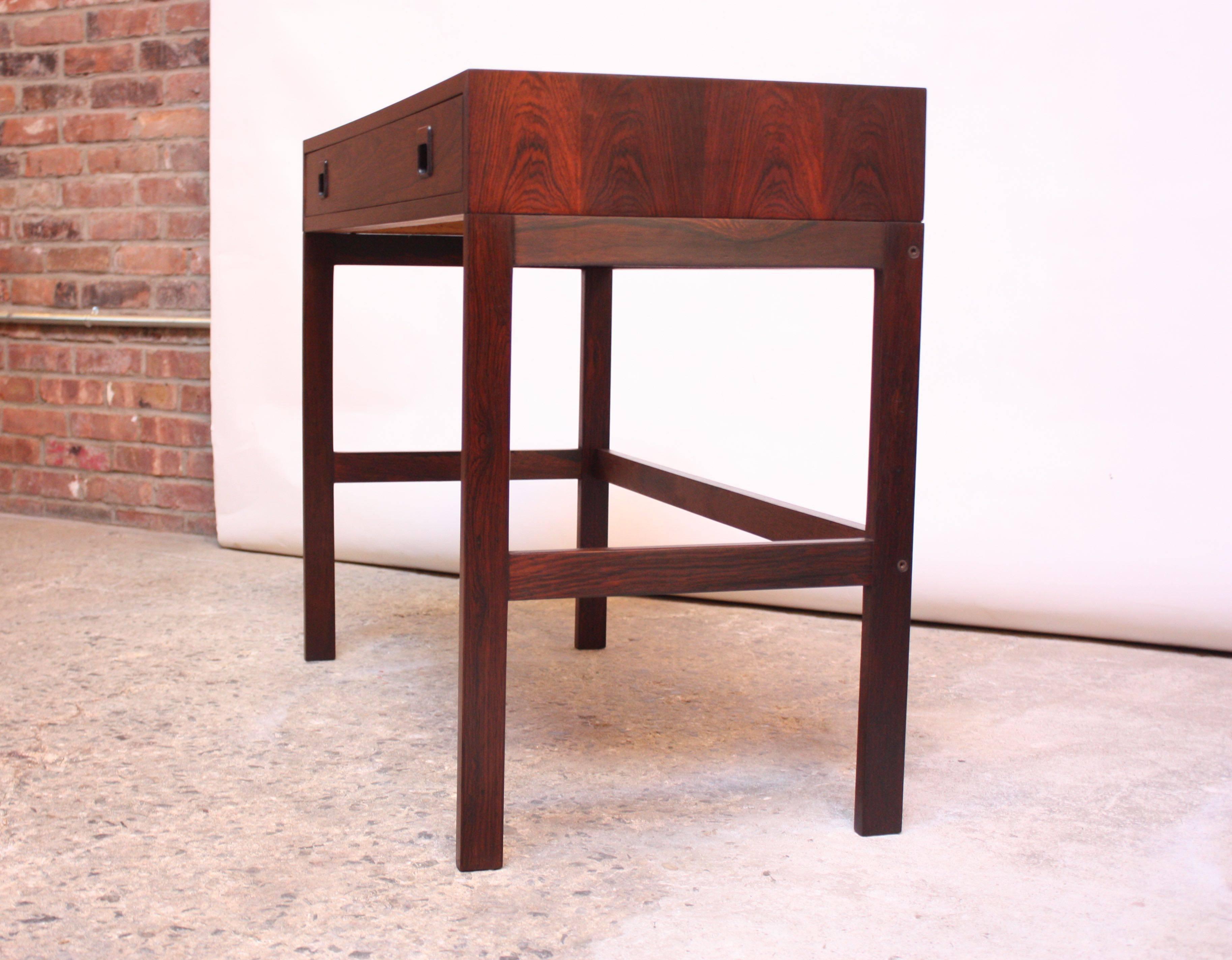 1960s Danish rosewood desk by EJM Skive Møbelfabrik. Elegant, minimal design with exquisitely book-matched top. Composed of a single drawer with inset rosewood pulls. Top desk portion, braced by solid brass pegs, can be easily removed from the base
