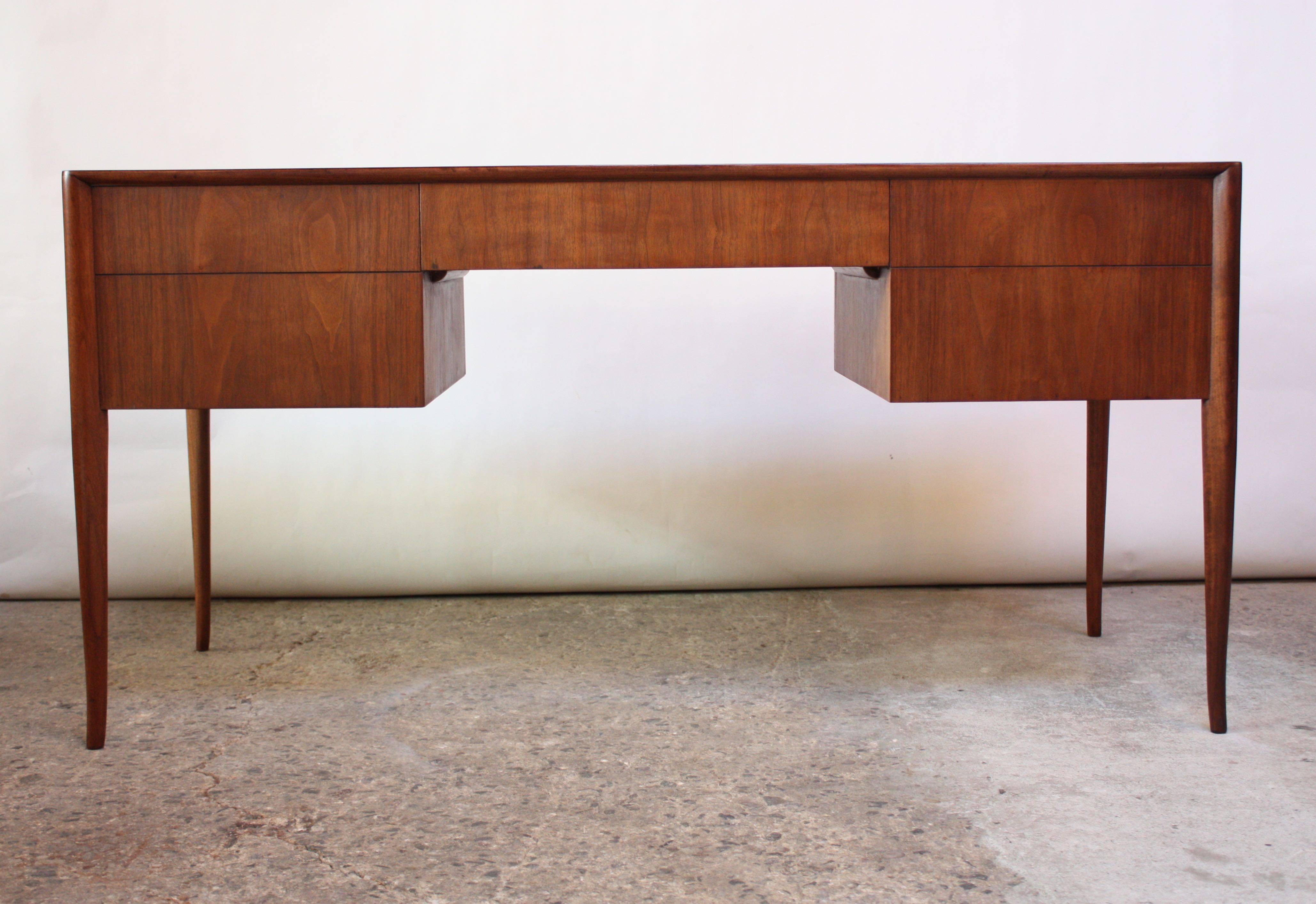 This walnut desk was designed by T.H. Robsjohn-Gibbings for Widdicomb in the 1950s. It is finished on both sides and features two large drawers on either side and a shallow drawer in the middle. Lovely walnut grain and rich color, expertly restored