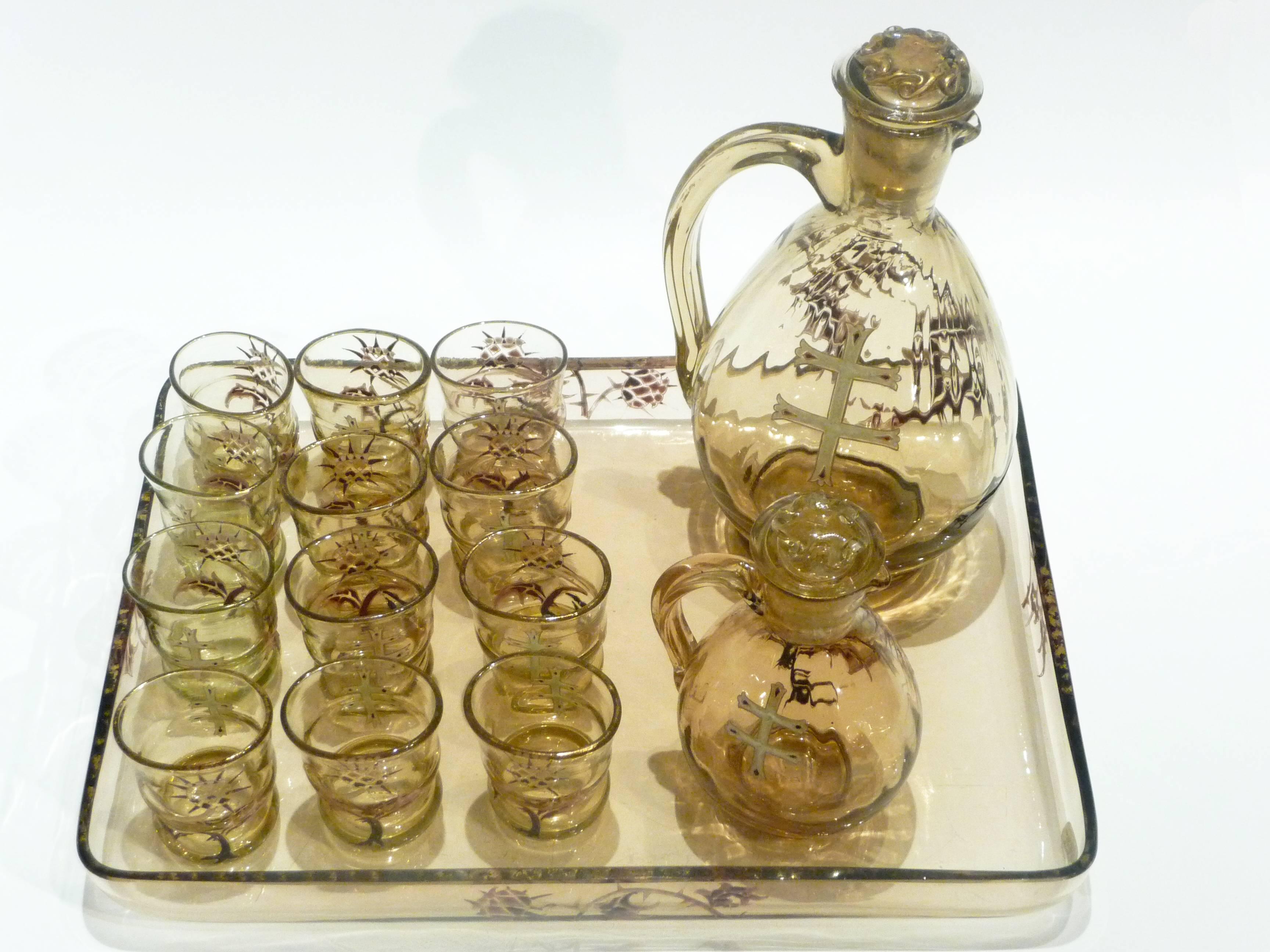 Emile Gallé
An Art Nouveau liqueur service
Including two jugs and their stoppers, 12 small glasses and a tray.
Enameled smoked glass decorated with thistles and the Cross of Lorraine
Signed

Measure: Jug 20 cm high; 13 cm width
Jug 12.5 cm