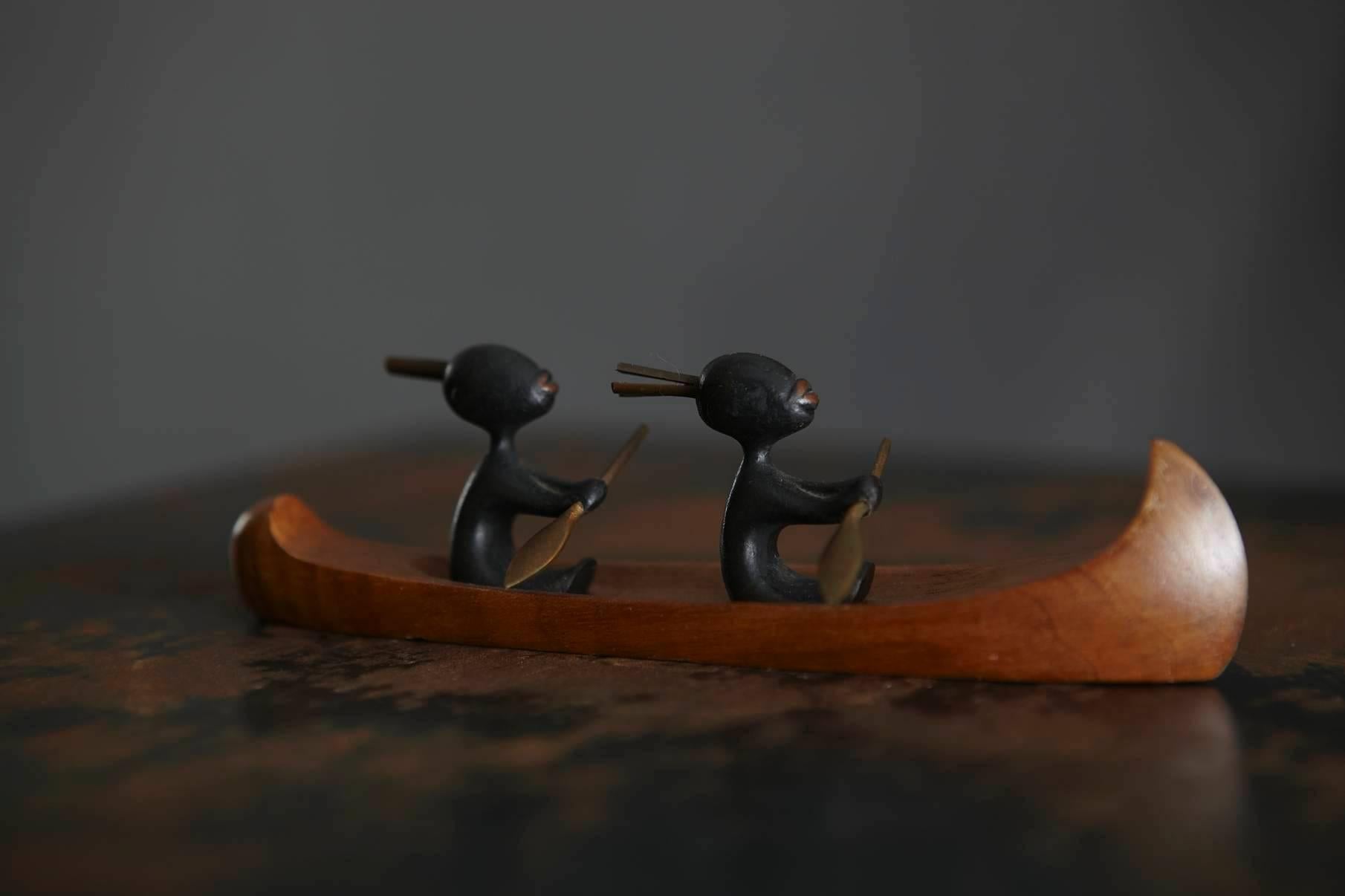 Two little African warriors in a wooden canoe, black patinated brass that has been partly polished to it's golden shimmer to highlight the oar, the headdress and the lips. The canoe is made out of tropical wood.
Marked on the bottom of the boat,