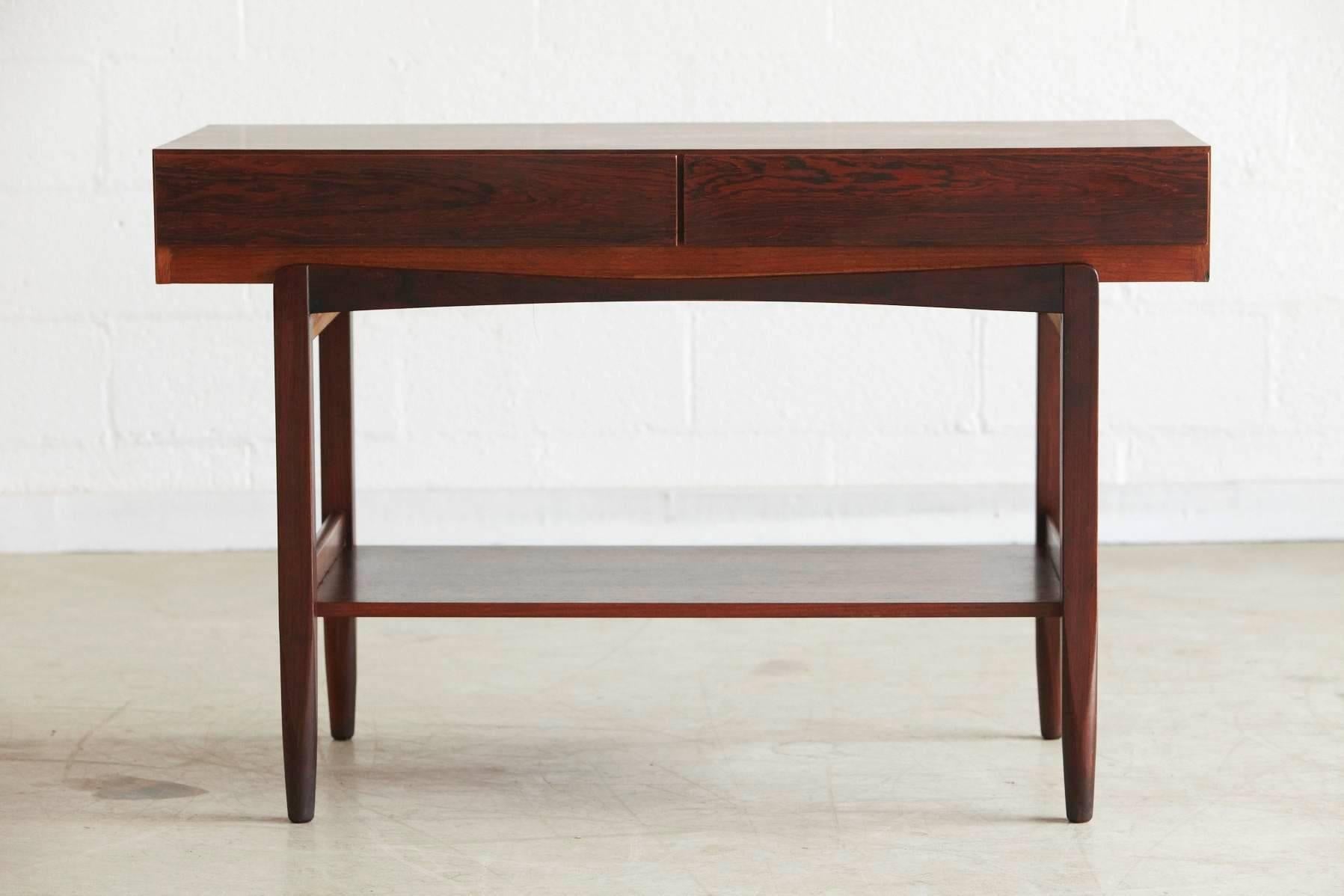 Elegant, minimalistic rosewood console table with two drawers with hidden pulls to the undersides and an under tier on slightly tapered legs. The pure, reduced lines of this piece are typical for Ib Kofod Larsen's design. The console table was