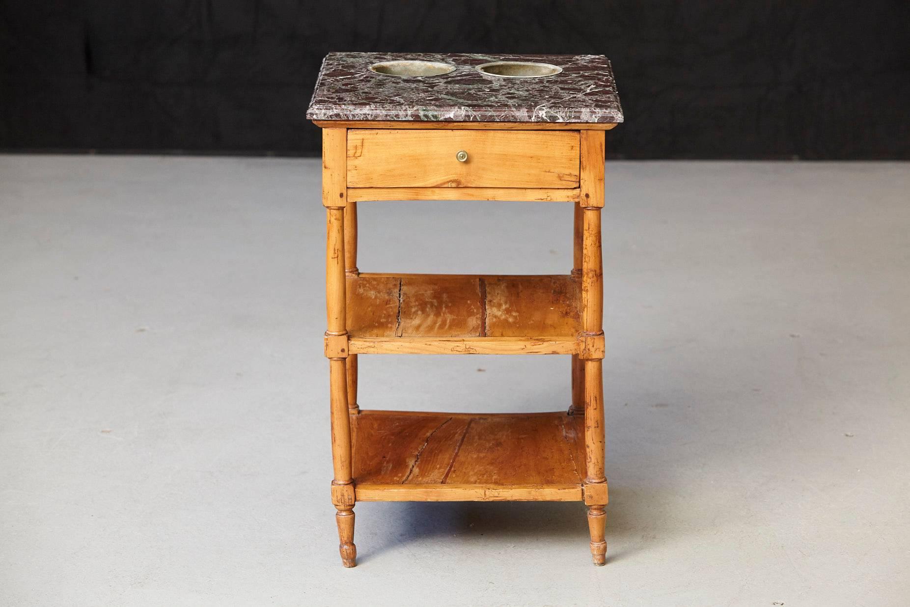 19th century French Provincial fruitwood work table having a square variegated grey and beveled marble top overhanging above a frieze with a single drawer, raised on turned columnar legs joined by two shelf stretchers.
The marble top has two zinc