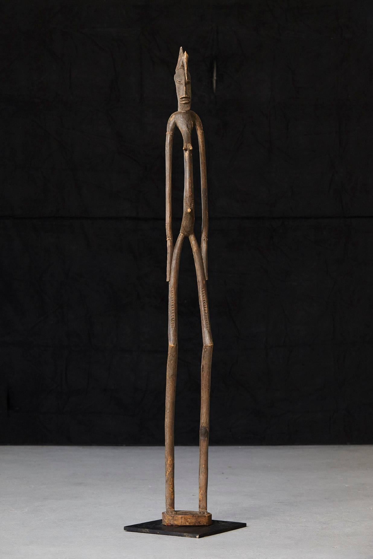 Carved African wood sculpture of a woman executed in a spindle pole formation with a curved torso, delineated breast and umbilicus. Arms and legs of tall narrow poles. A stork surmounting the head which is raised on a narrow neck. Three carved toes