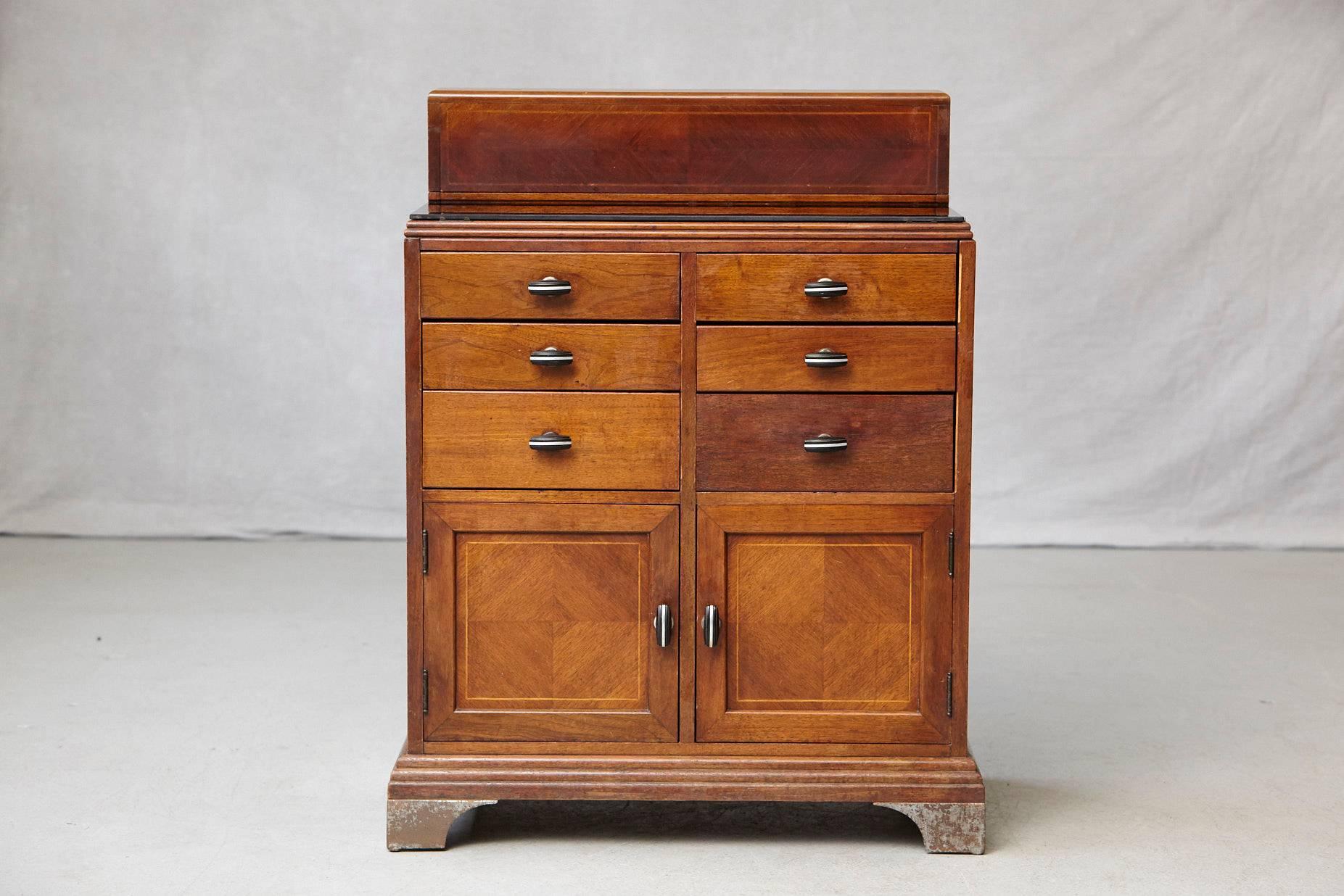 This rare 1930s walnut medical cabinet or dental station with plenty of beautiful details was manufactured by W.D. Allison Co., Indianapolis and distributed by National Surgical Stores Inc, Brooklyn.
This cabinet is raised on four chromed metal