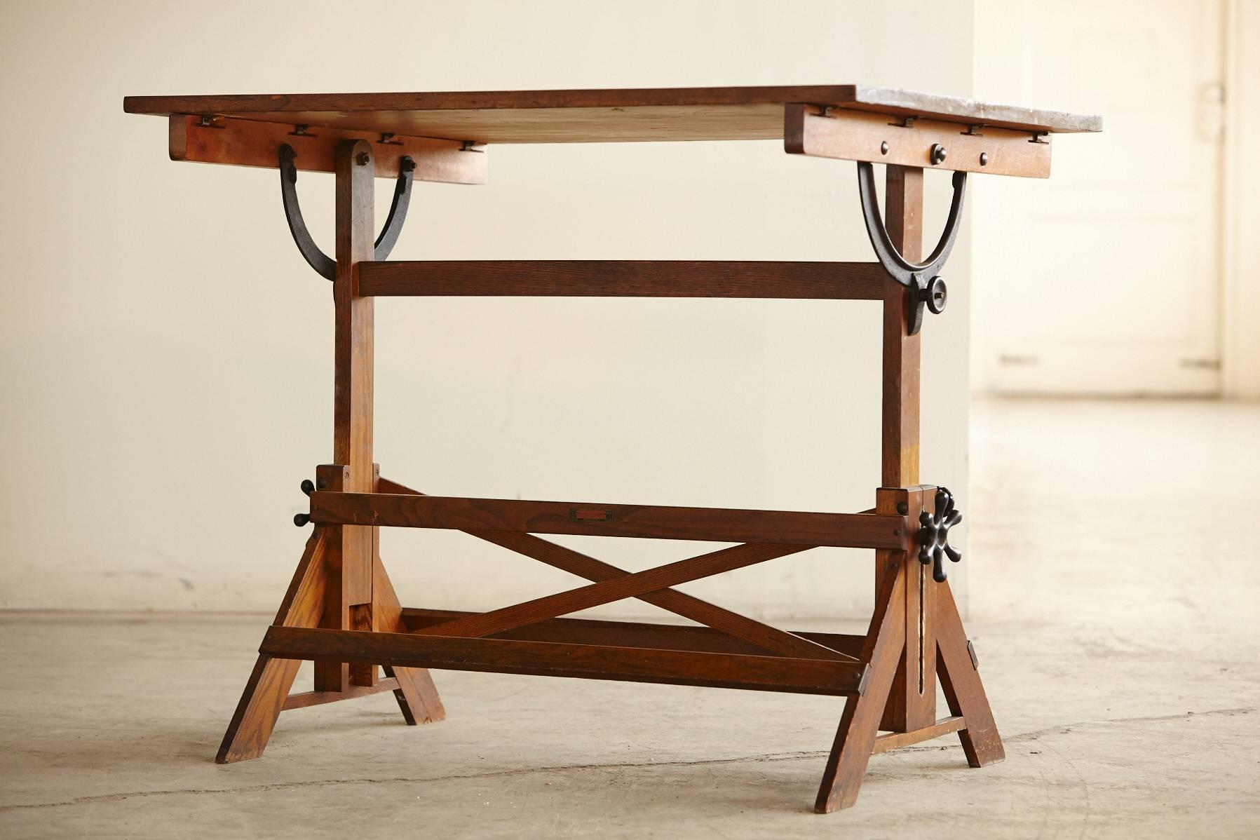 Antique Industrial American oak drafting or drawing table with cast iron hardware, adjustable height and tilt.
Beautiful patinated, distressed appearance, solid and sturdy construction.
Adjustable height from 28