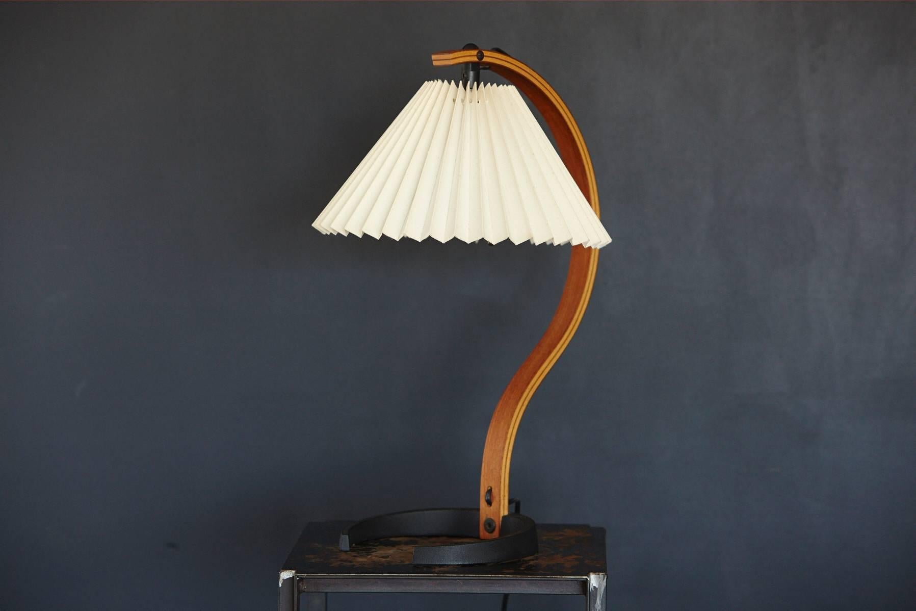 Bentwood table lamp with original pleated lampshade designed by Mads Caprani. Beautiful fluid, sculptural birch frame embracing the cream colored pleated, accordion lamp shade and ending in a crescent shaped black cast iron base. Original sticker