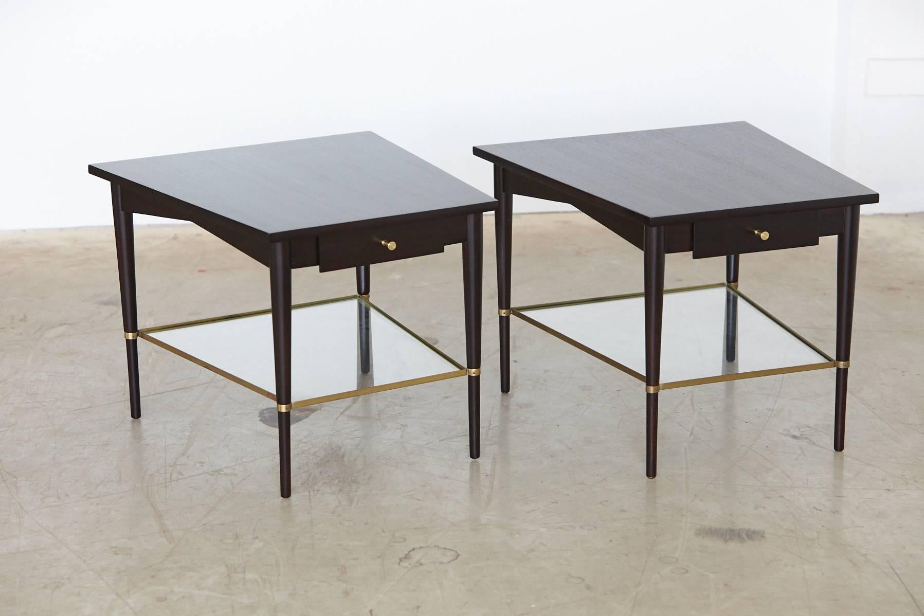 Elegant and very rare pair of trapezoidal ebonized end or side tables with brass frames and glass shelves. The drawers are equipped with the signature hourglass brass pulls.
The tables are from Paul McCobb's Connoisseur collection for H. Sacks &
