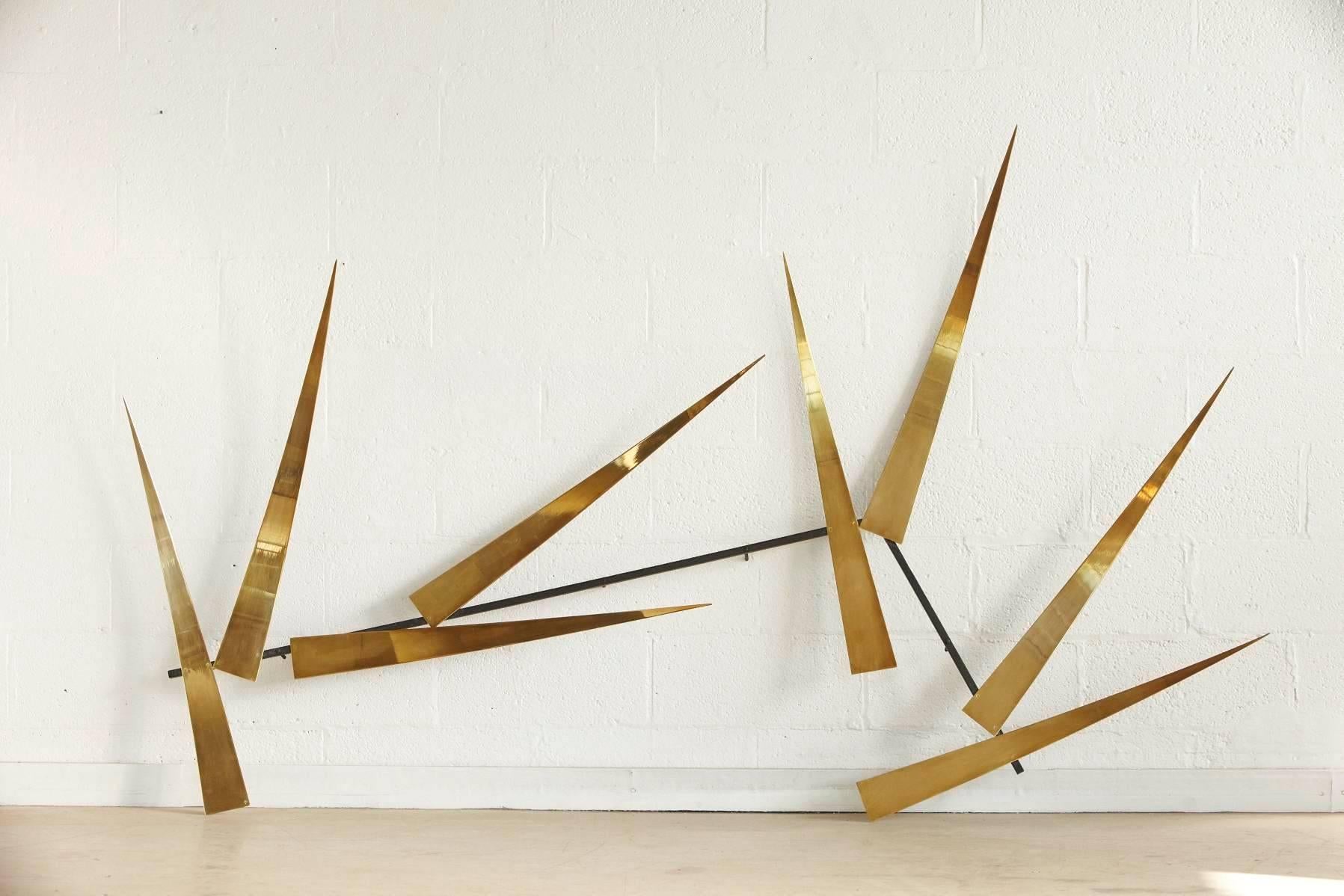 Large abstract brass wall sculpture by Joe Sorge, depicting brass flashes pointing in different directions, which can be interpreted as rays of sun when the light is reflecting in the brass from different angles or hung over a fire places they could