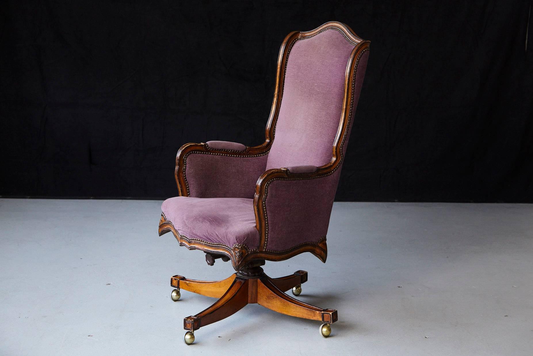 High quality early 1970s reproduction high back walnut 'banker's' chair on pastored swivel base and covered in nail trimmed violet striae velvet.
There is one piece of wood missing in the lower part of the swivel base between two legs of the chair,