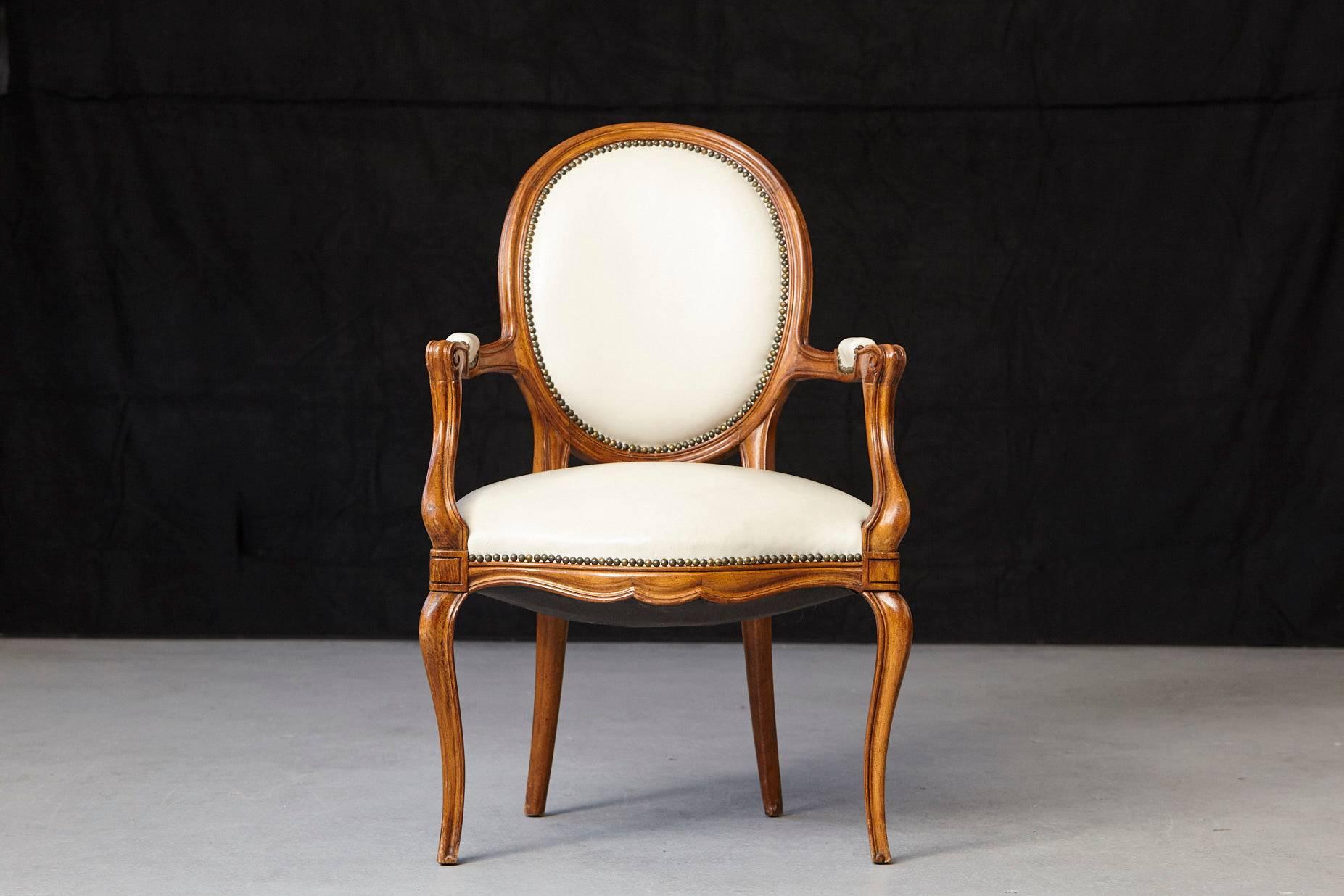 Gorgeous Louis XV style fauteuil with a molded walnut frame, having an oval back and shaped seat covered in nail trimmed creme leather and with conforming elbows rests on the shaped arms. The arms with voluted supports, shaped apron, the whole
