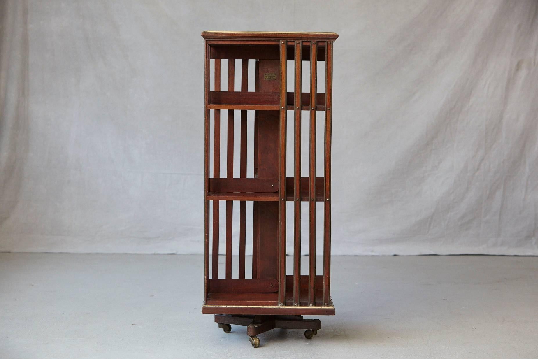 Antique French revolving mahogany bookcase with beautiful brass details, brass trim around the top and bottom, aligned brass screws and raised on four brass casters. Two tiers having slated upright supports. Nice patinated brass.
Original brass