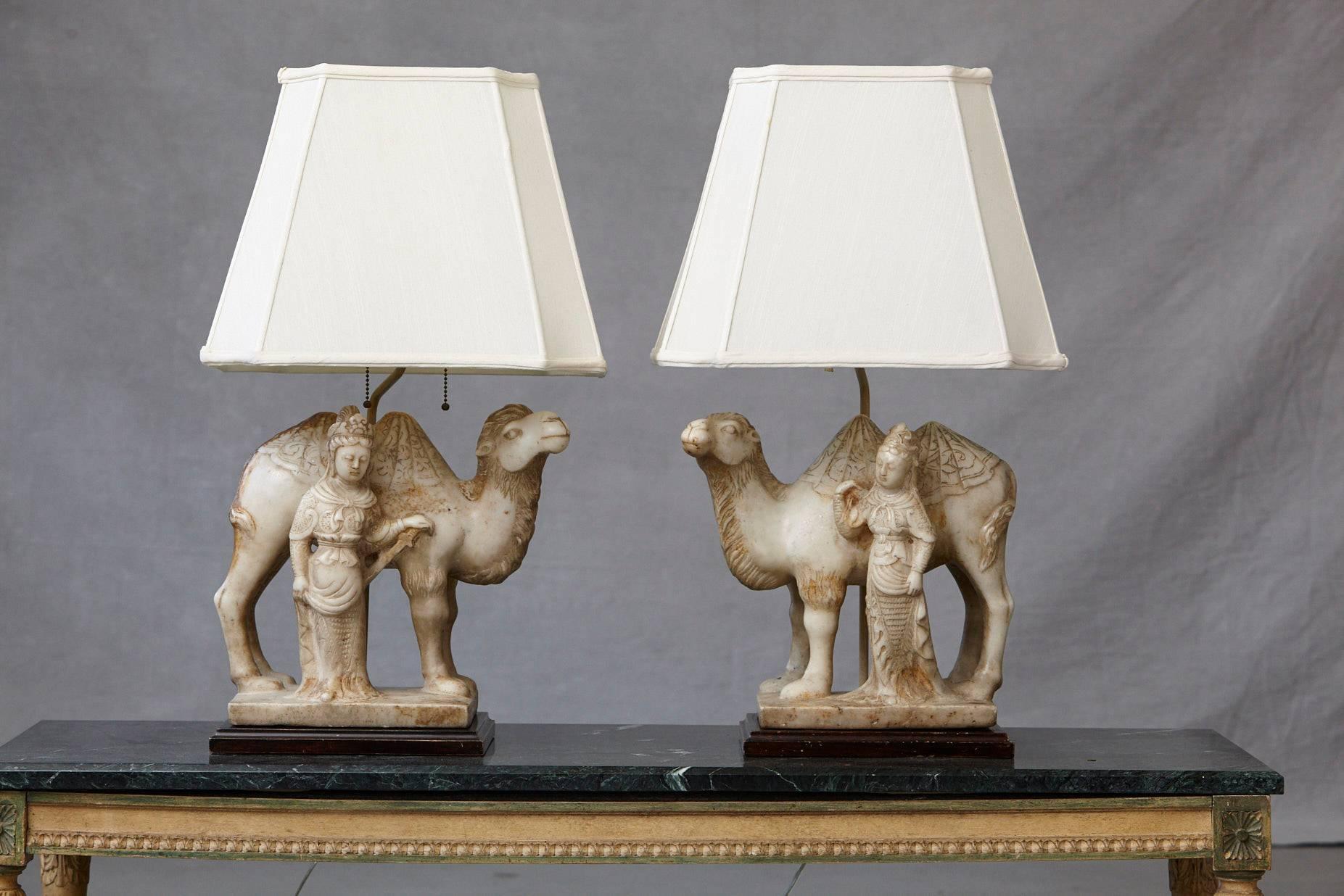 Impressive pair of detailed hand-carved figurative marble table lamps depicting each an Asian woman in front of a dromedar facing each other, raised on rosewood bases, with custom-made height adjustable rectangular silk shades.

The inner lining